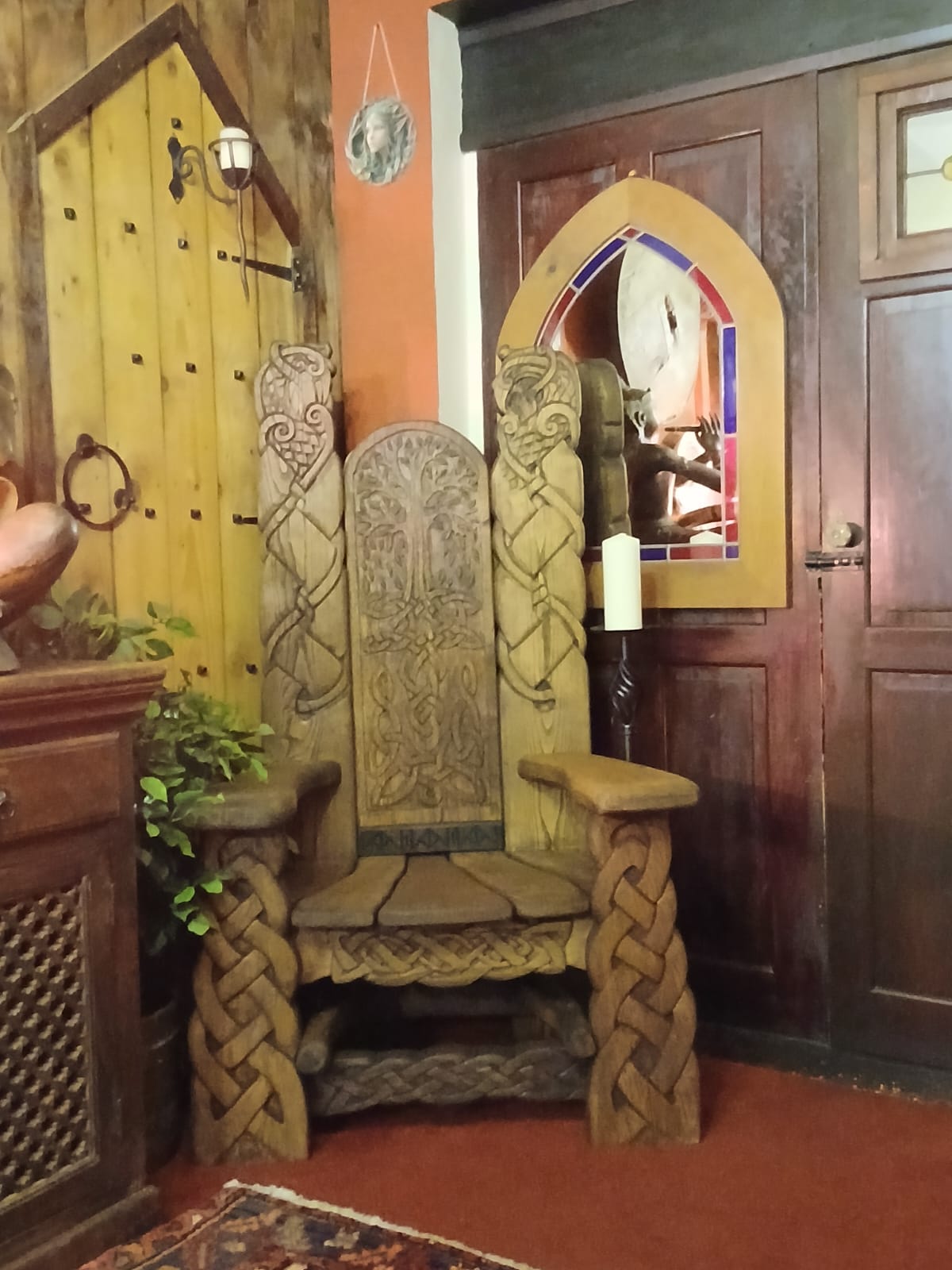 Hand-carved Viking storytelling chair in oak with intricate knotwork and tree of life design, placed indoors with plants and warm lighting — a bespoke wooden chair worth every penny.