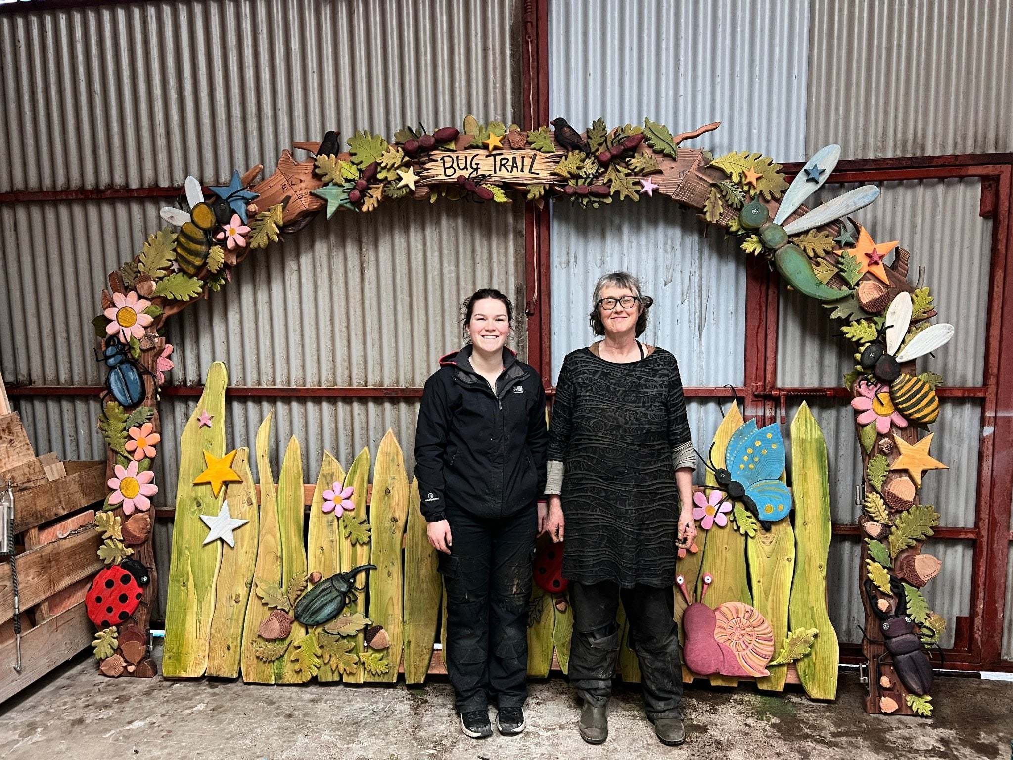 Two people standing in front of a decorative arch with floral and insect designs.