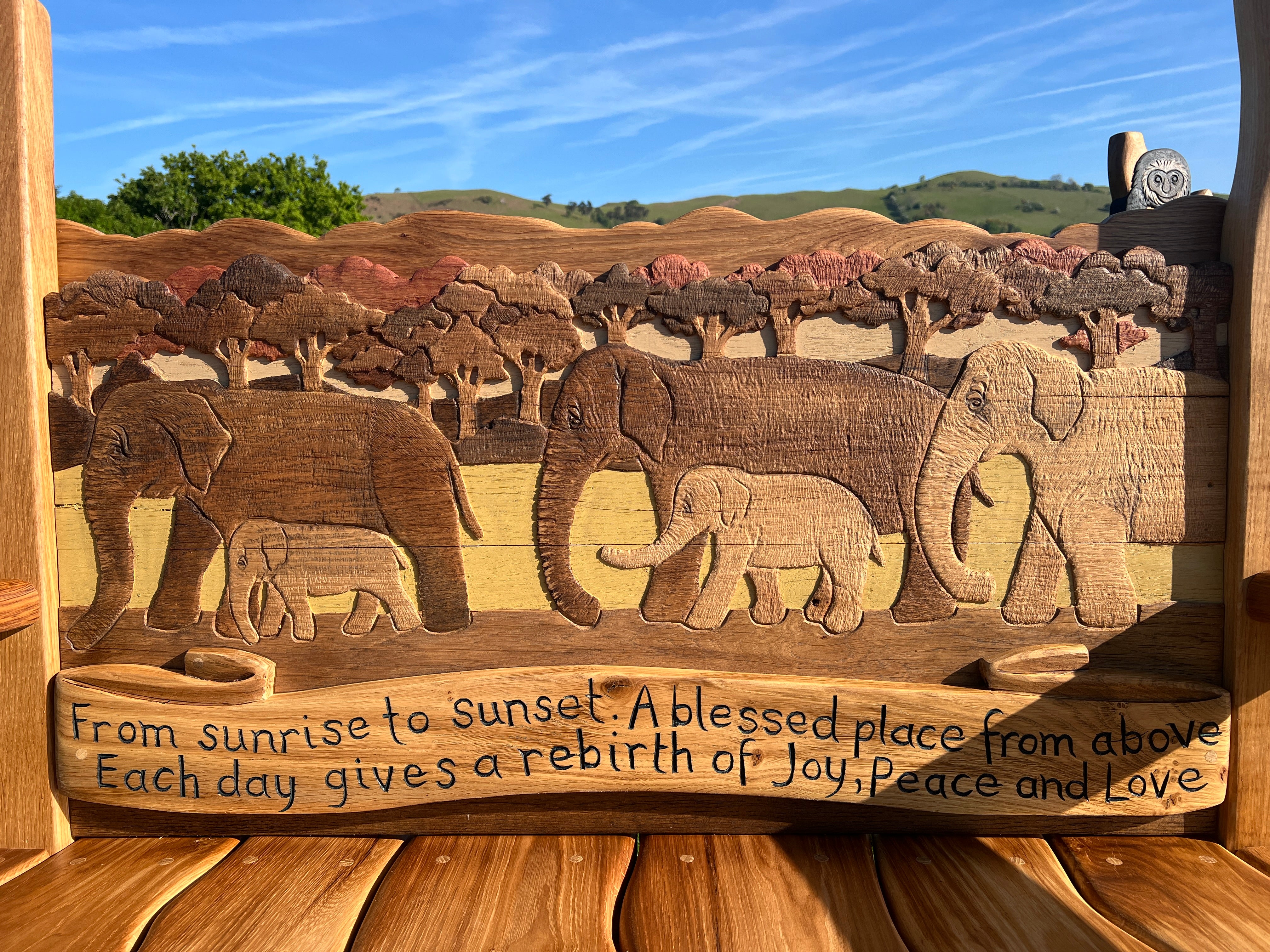 Close-up of elephant carving and engraved message on backrest of bespoke oak memorial bench.