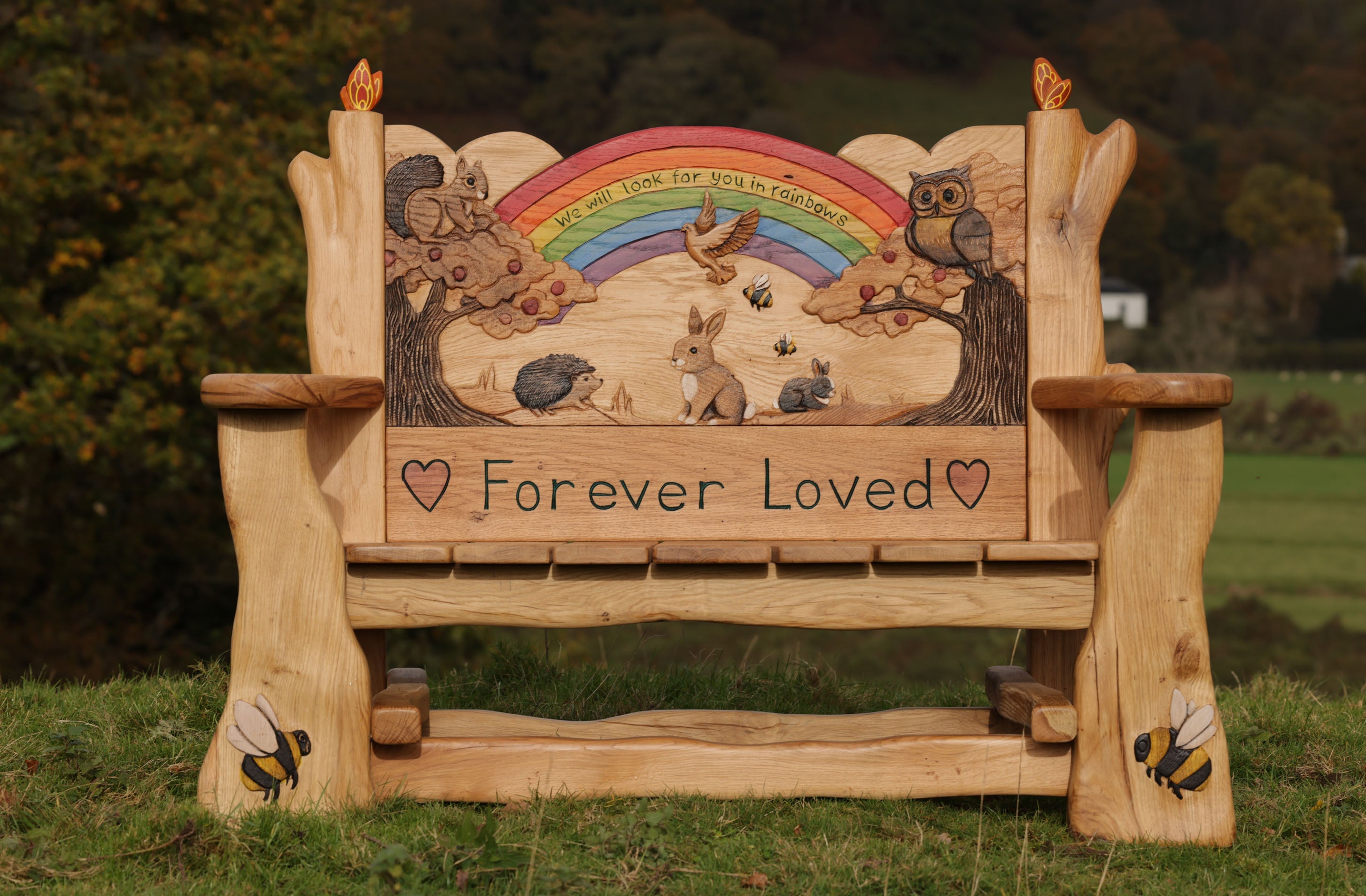 Wooden bench with animal illustrations and 'Forever Loved' text in a natural setting