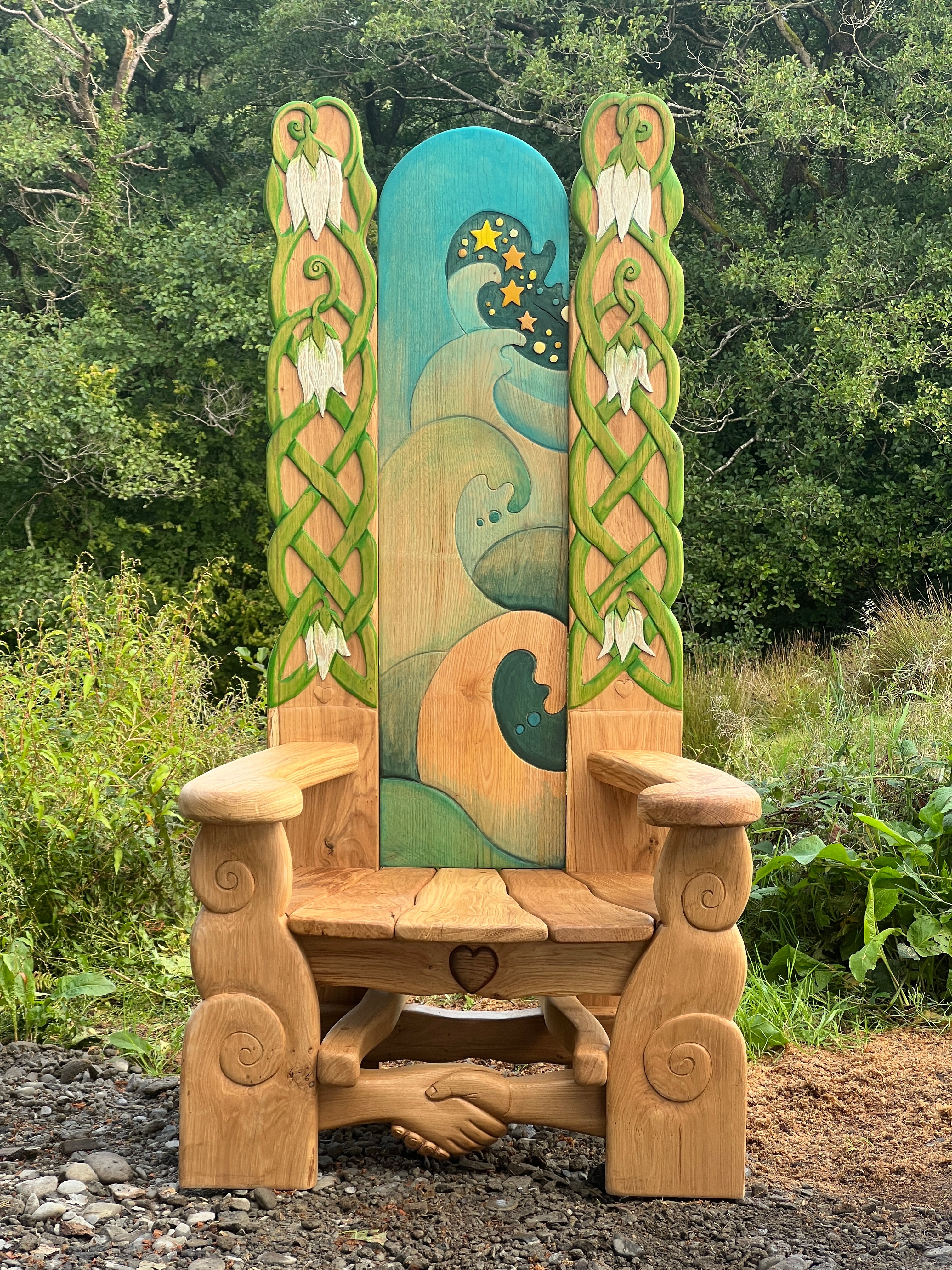 Oak storytelling chair with handshake carving and painted design, photographed outdoors in woodland