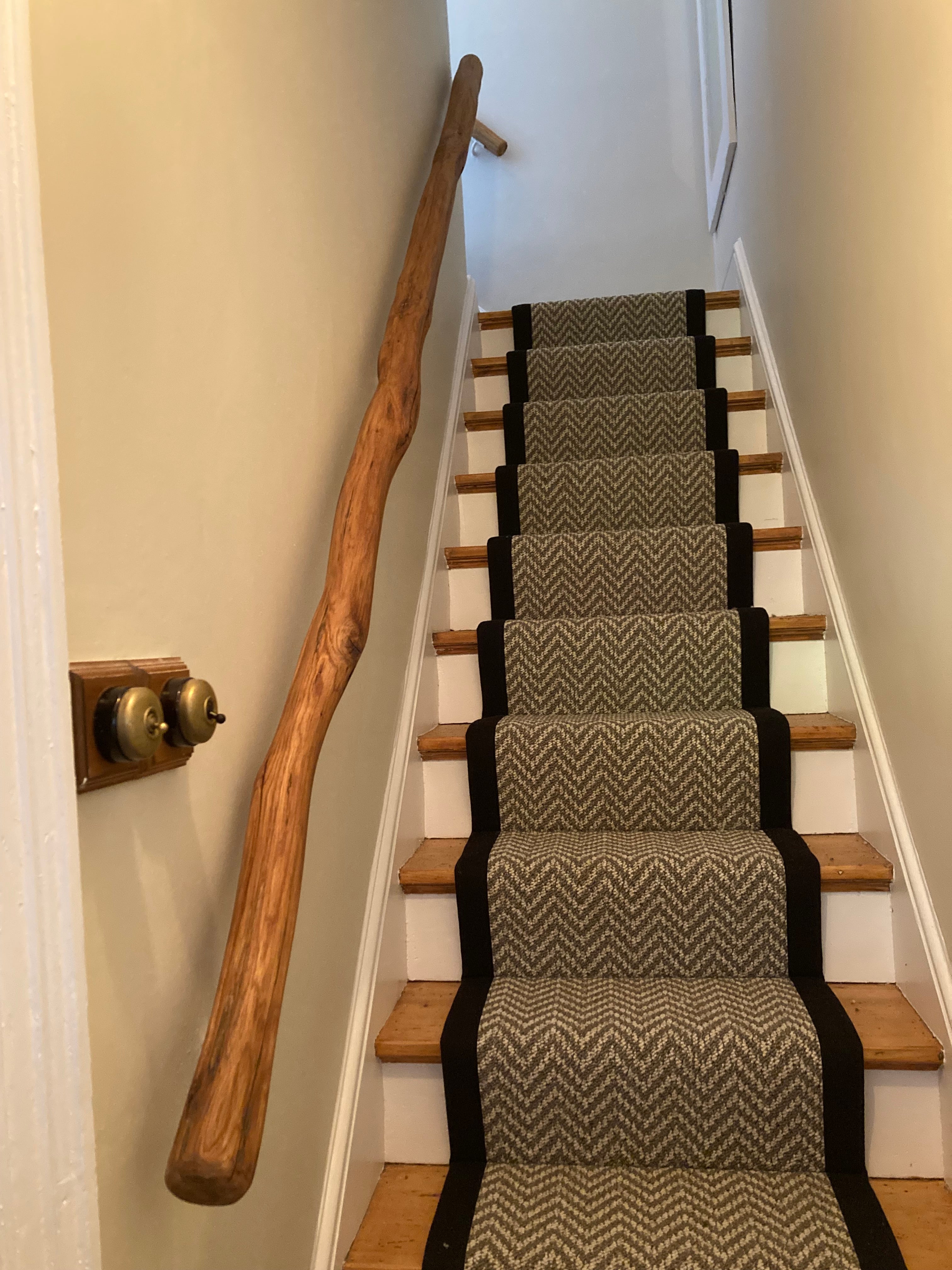 Handcrafted natural wood stair handrail with rustic finish installed along carpeted staircase