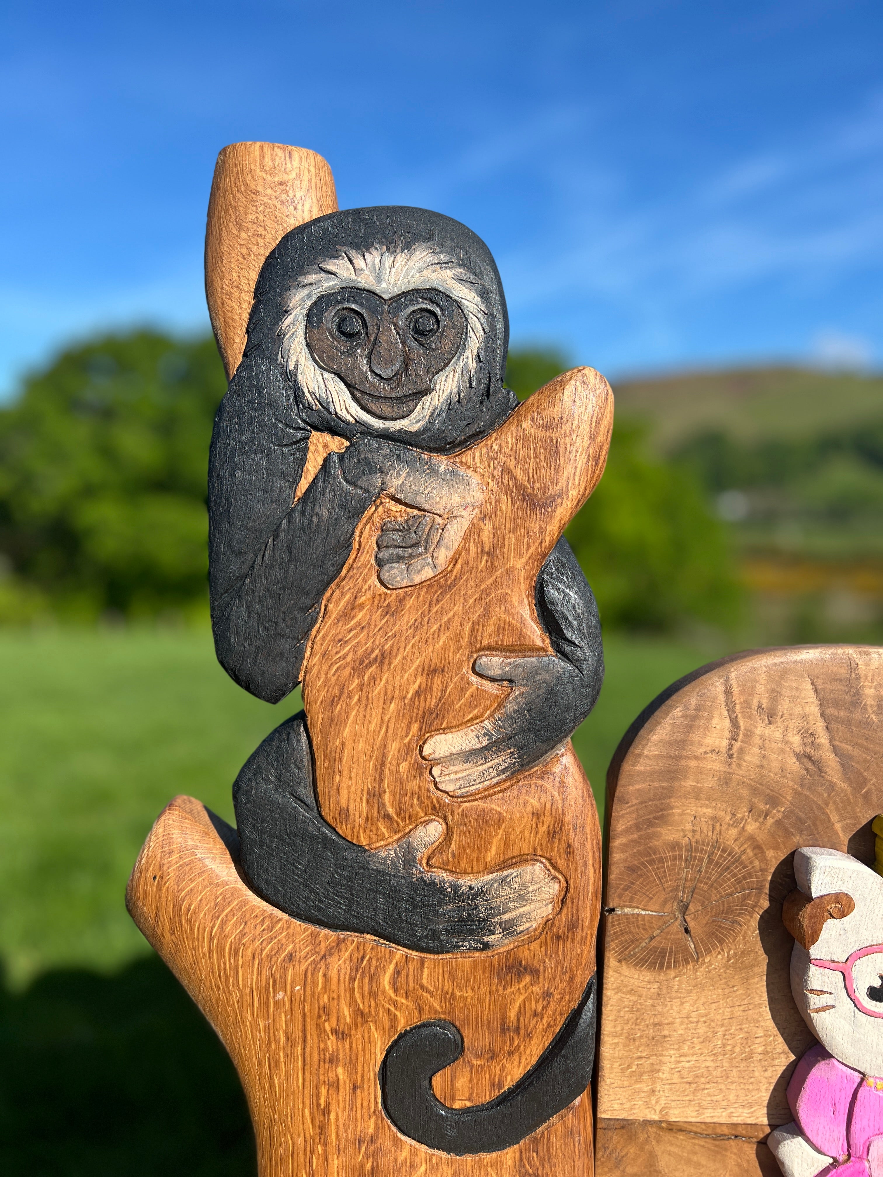 Close-up of carved and painted monkey clinging to a tree branch, part of the armrest design on a custom children’s memorial bench in oak.