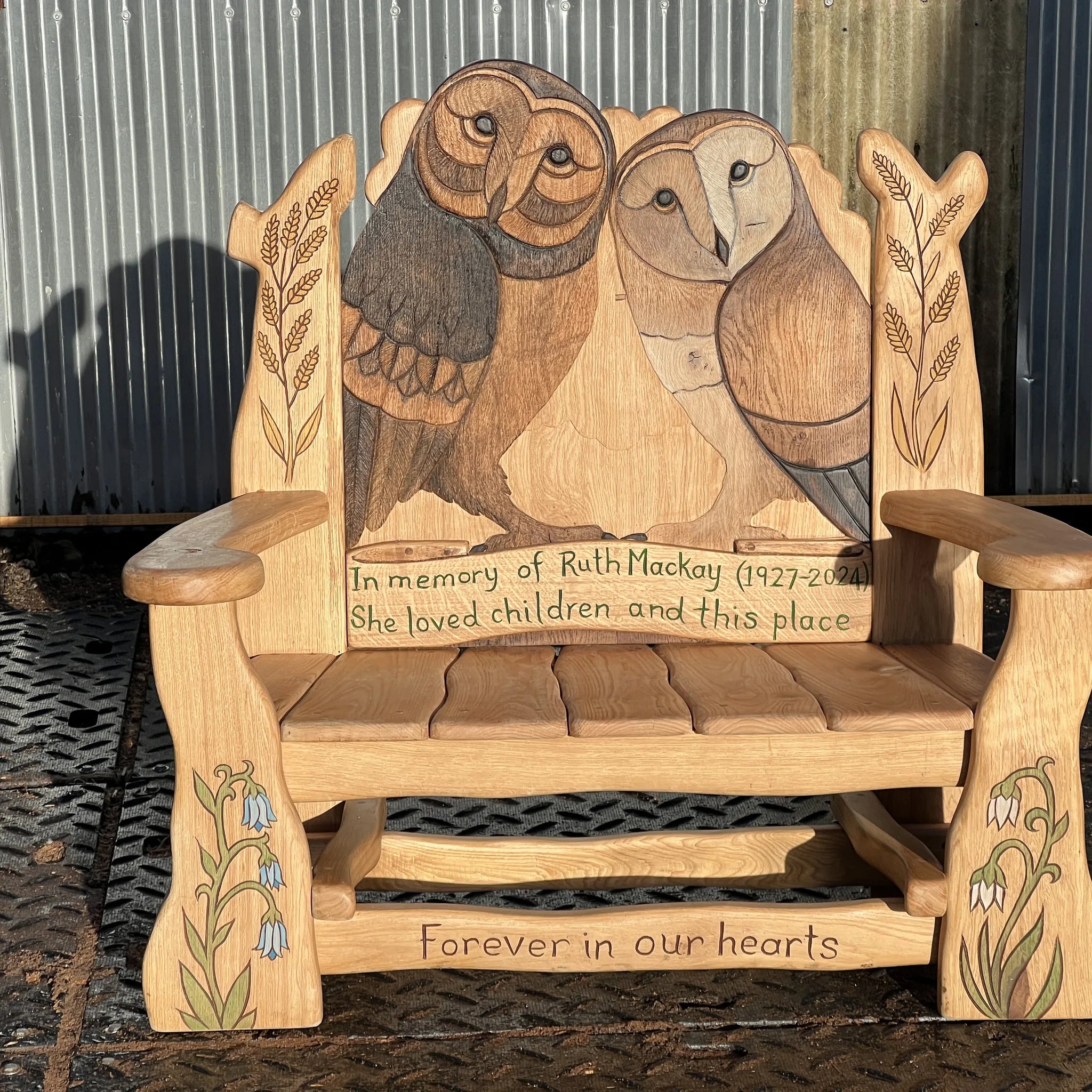 Hand-carved solid oak memorial bench with two painted barn owls, wheat sheaves and snowdrops — bespoke commission by FreeRangeDesigns