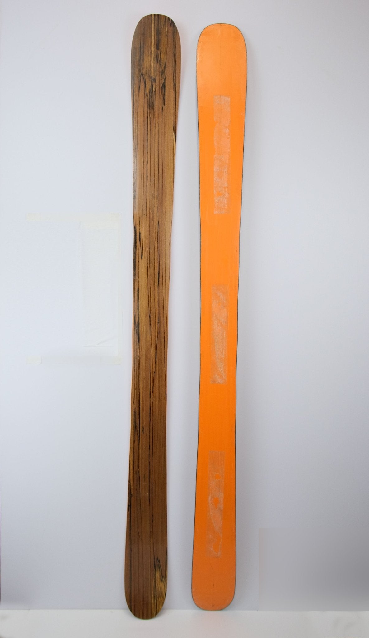 Pair of Powder Playfull 117 skis laid flat, showing the spalted beech woodgrain topsheet on one ski and the bright orange base on the other, displayed side-by-side against a plain white background.