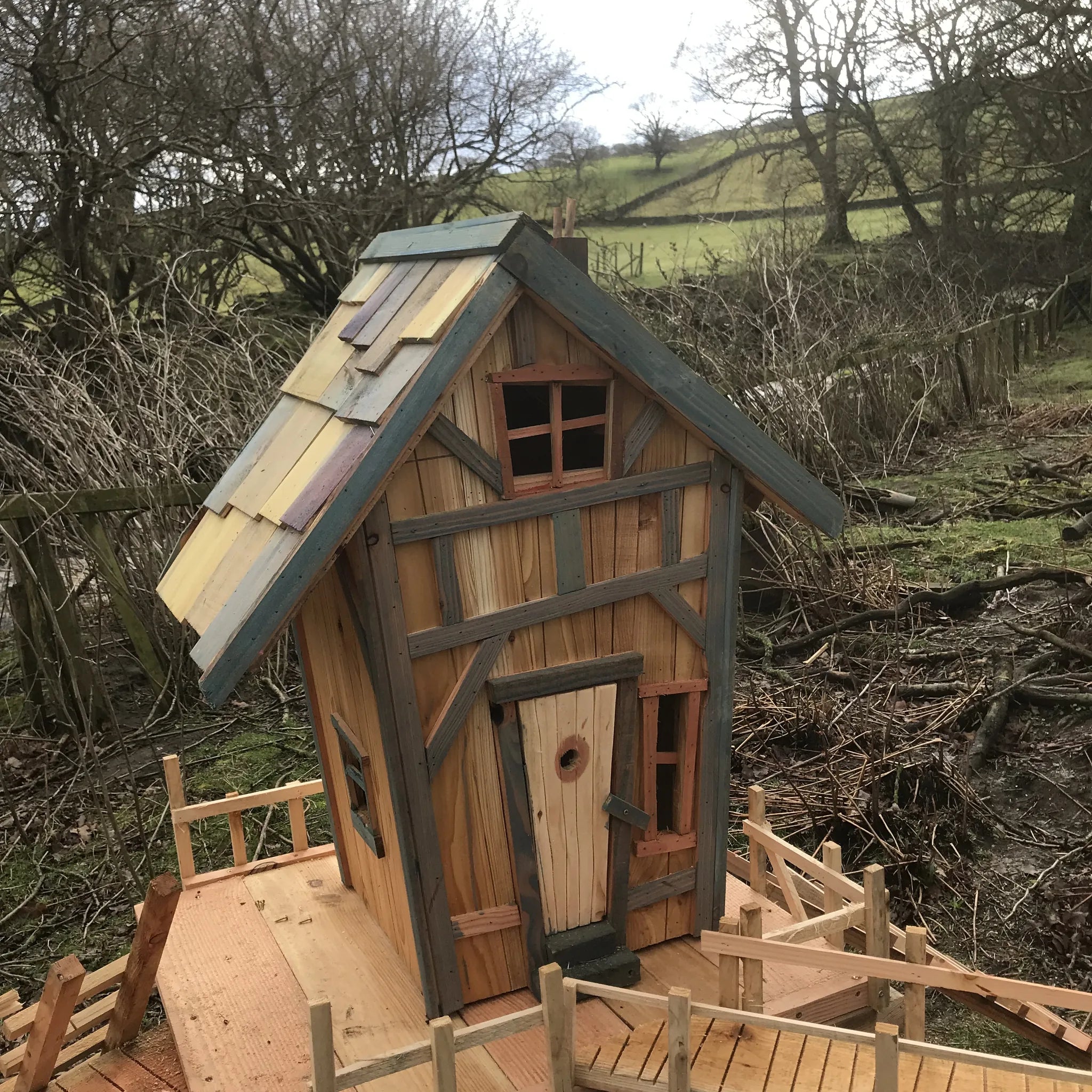 Handmade rustic treehouse fairy house with bark-on branch supports, wooden platforms and natural wood ladder