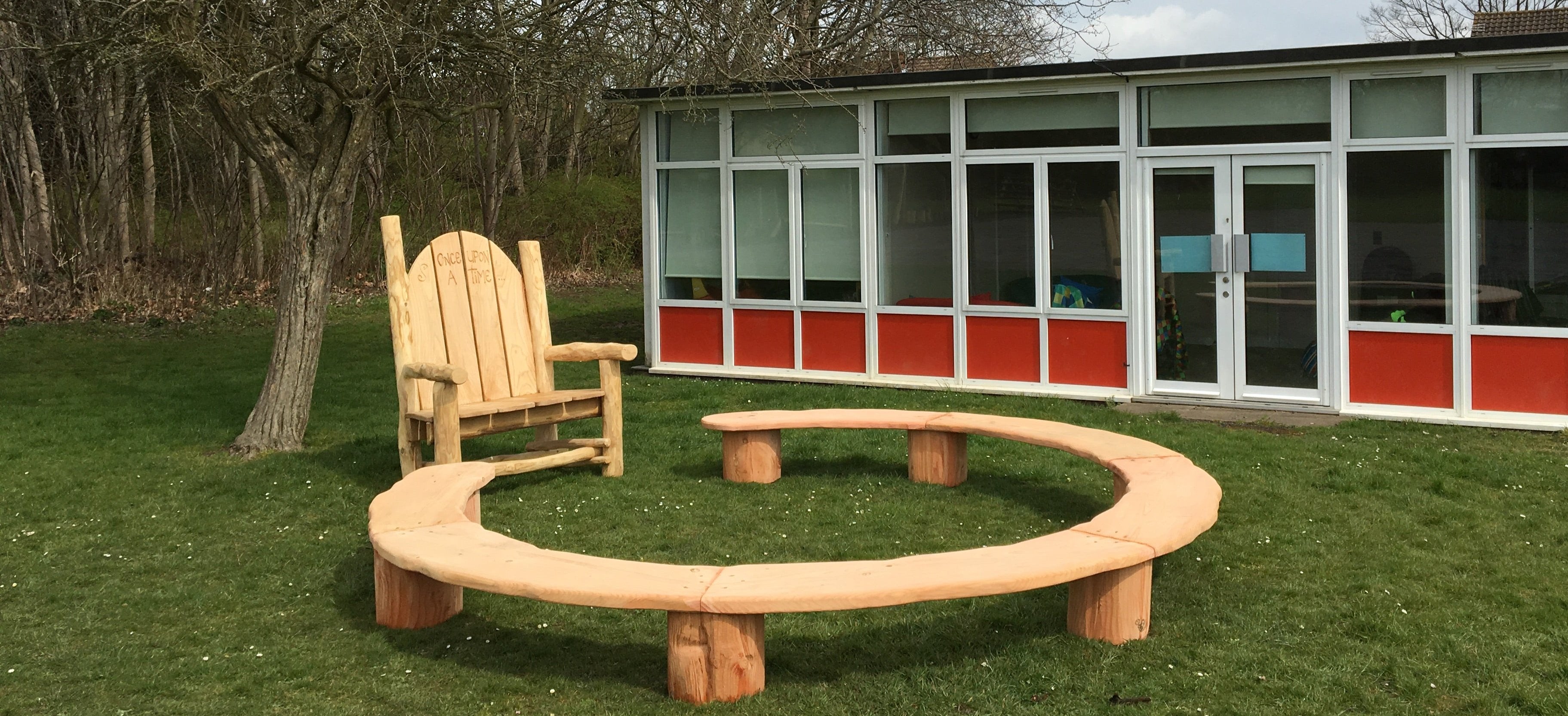 Outdoor storytelling ring seating arrangement for schools featuring a large rustic 'Once Upon A Time' storytelling chair and curved wooden benches, perfect for engaging group activities and interactive learning sessions