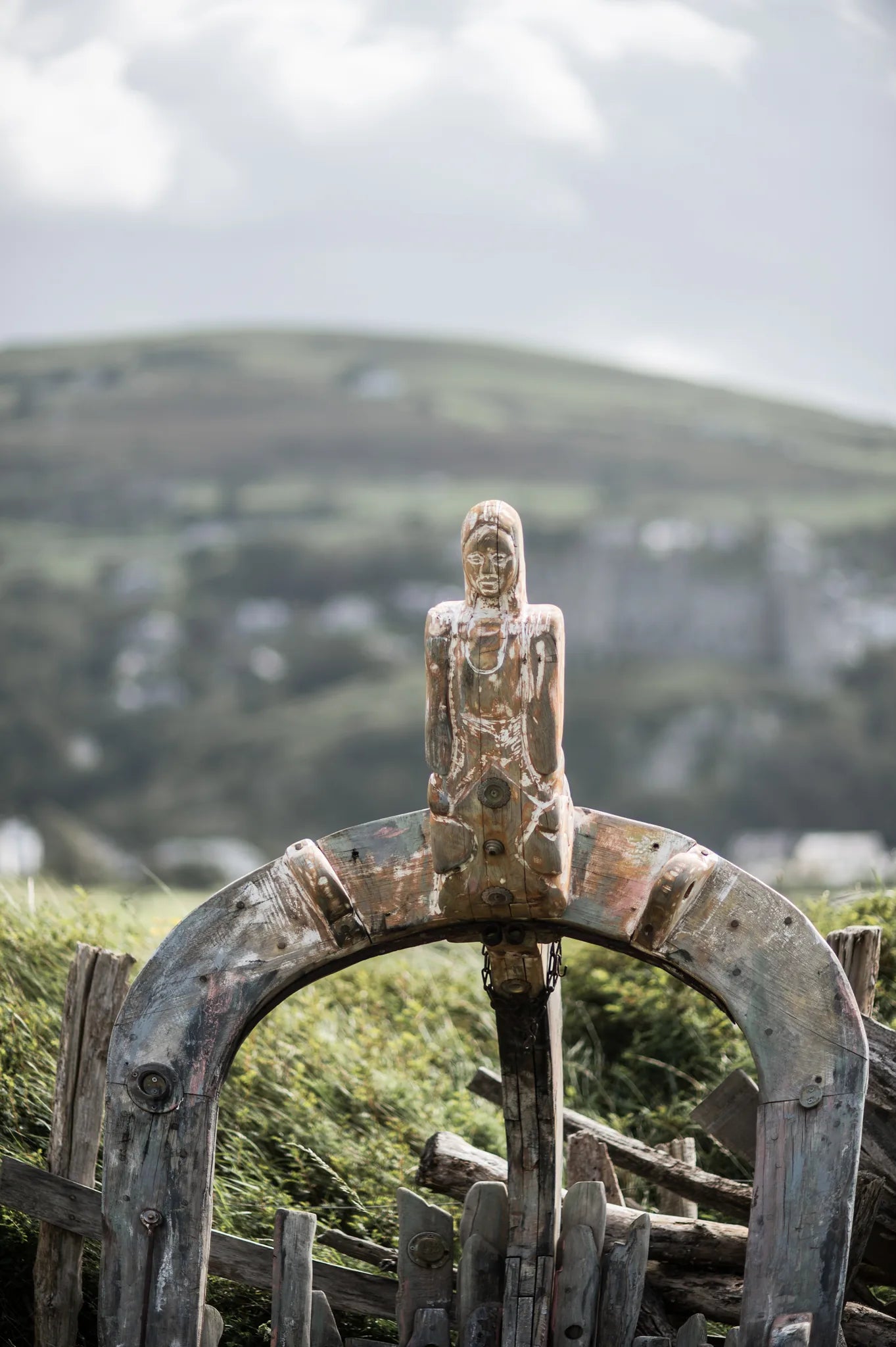 Front view of the Shipwreck storytelling chair in solid oak | carved figurehead centred on arch | Welsh hills behind