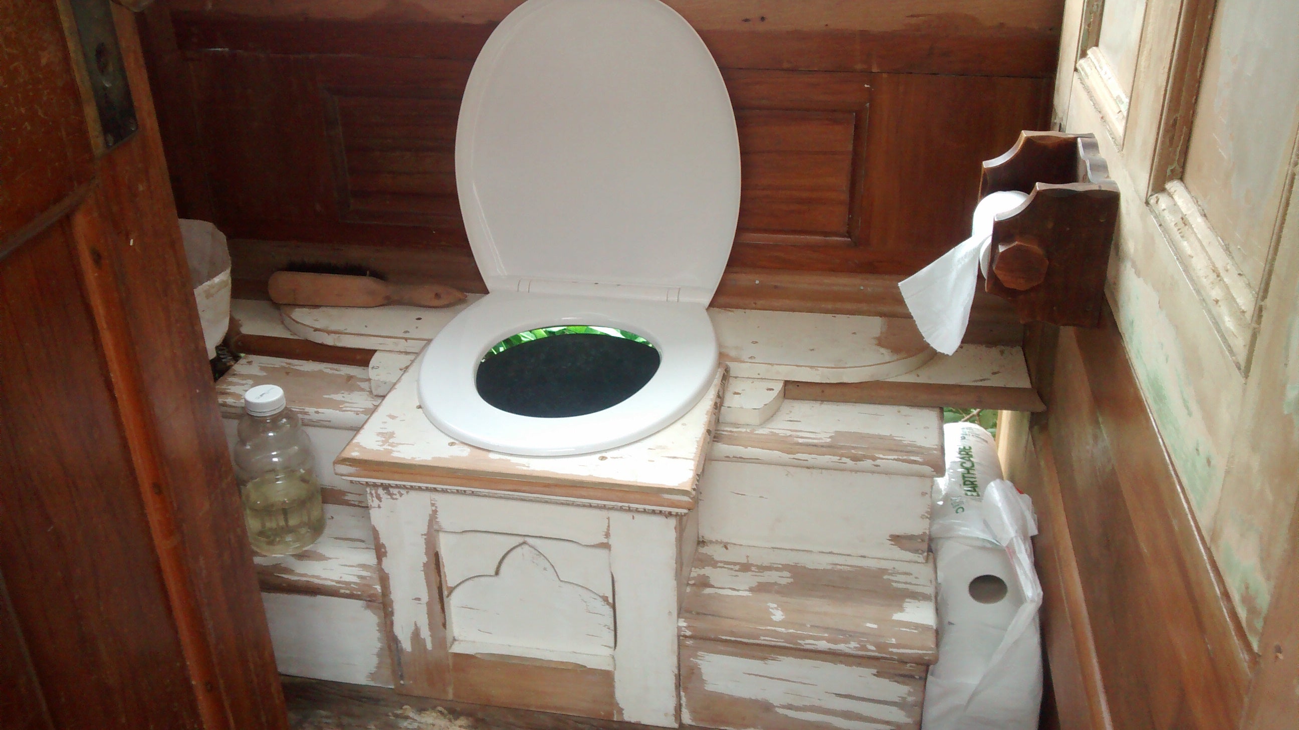 Rustic compost toilet installation in wooden setting.