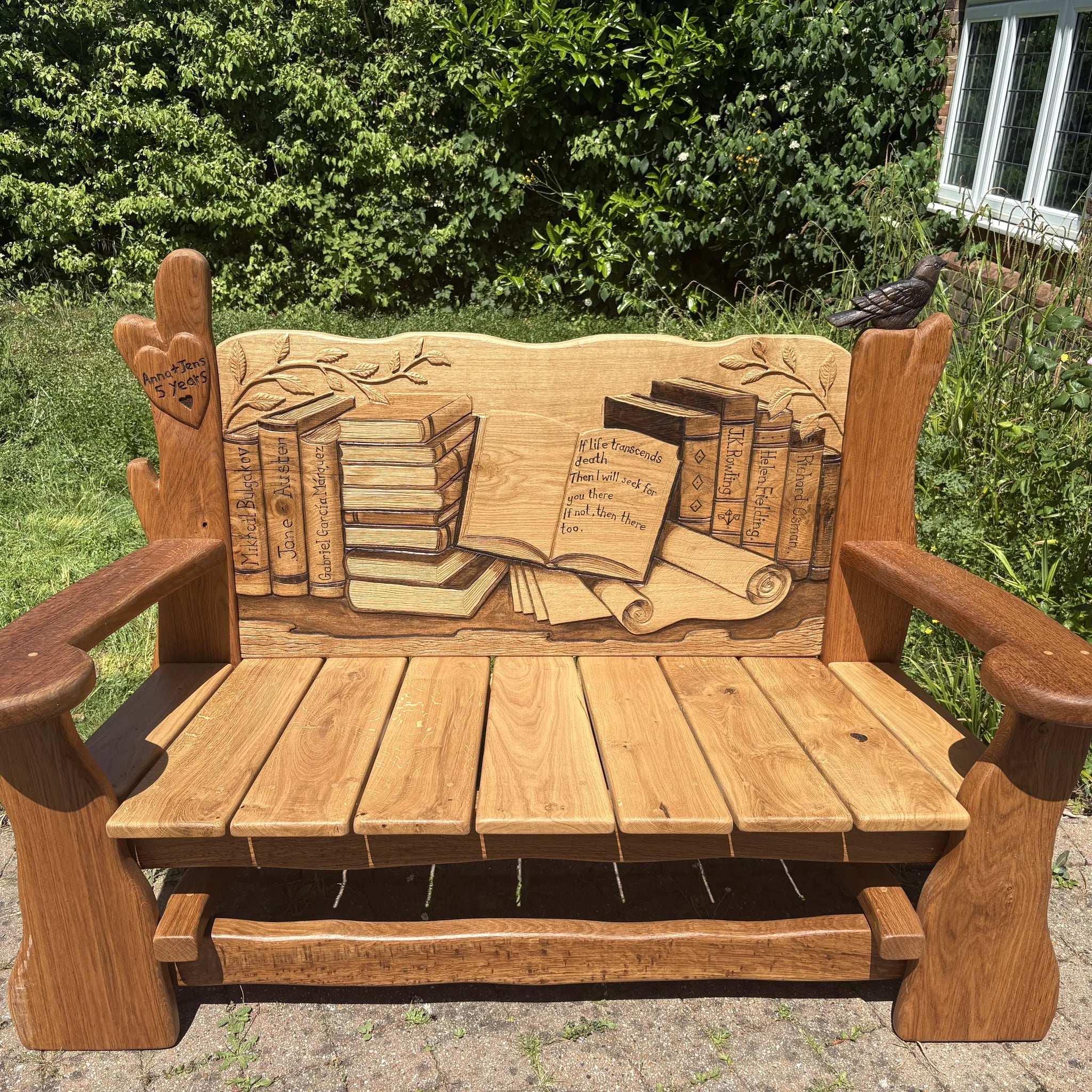 Hand-carved solid oak book lover's bench in a garden, with carved books, a scroll and an open book