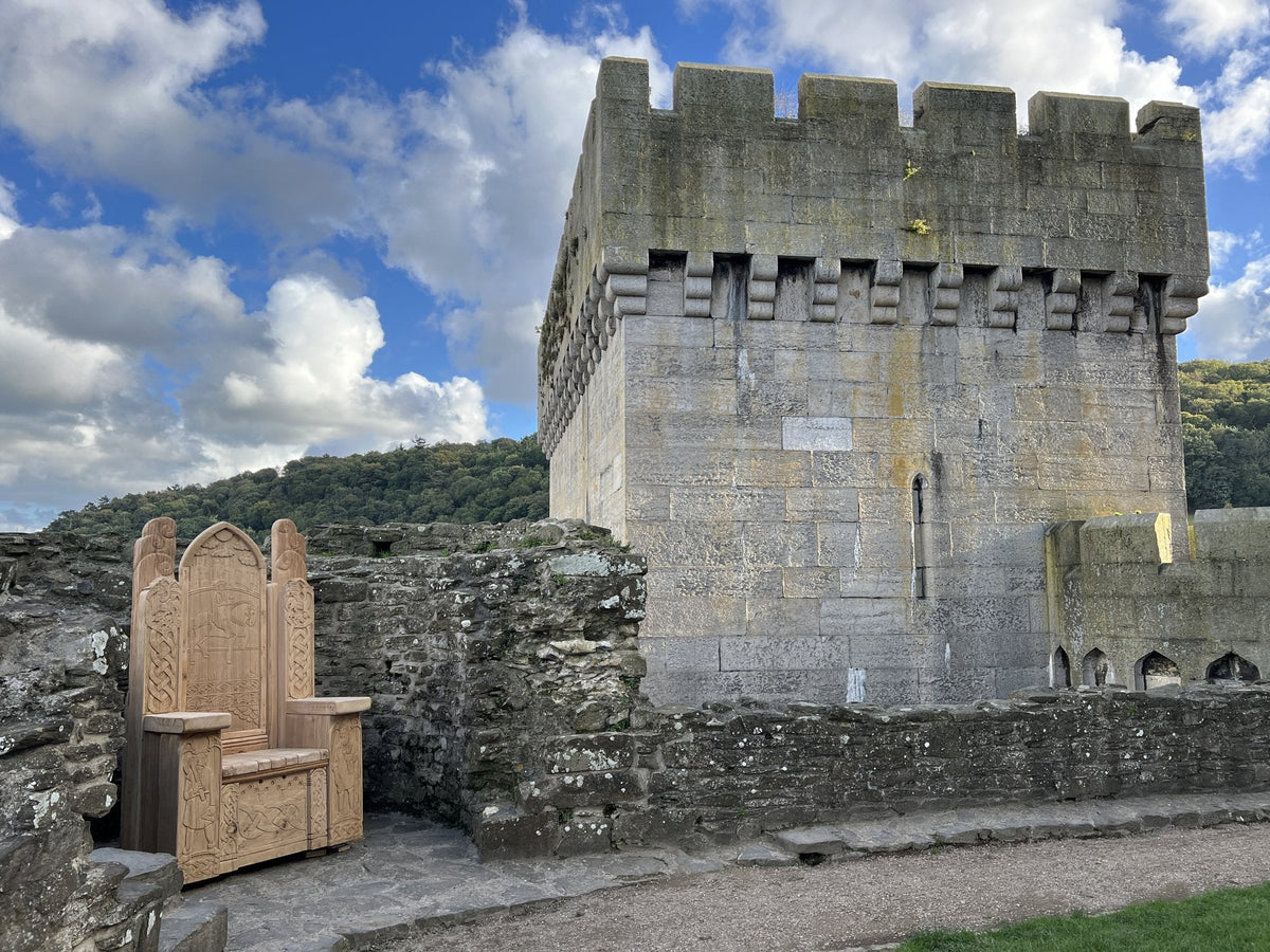 Hand-carved solid oak throne beside a tower on the walls of Conwy Castle — sculptural seating commission for Cadw by Free Range Designs
