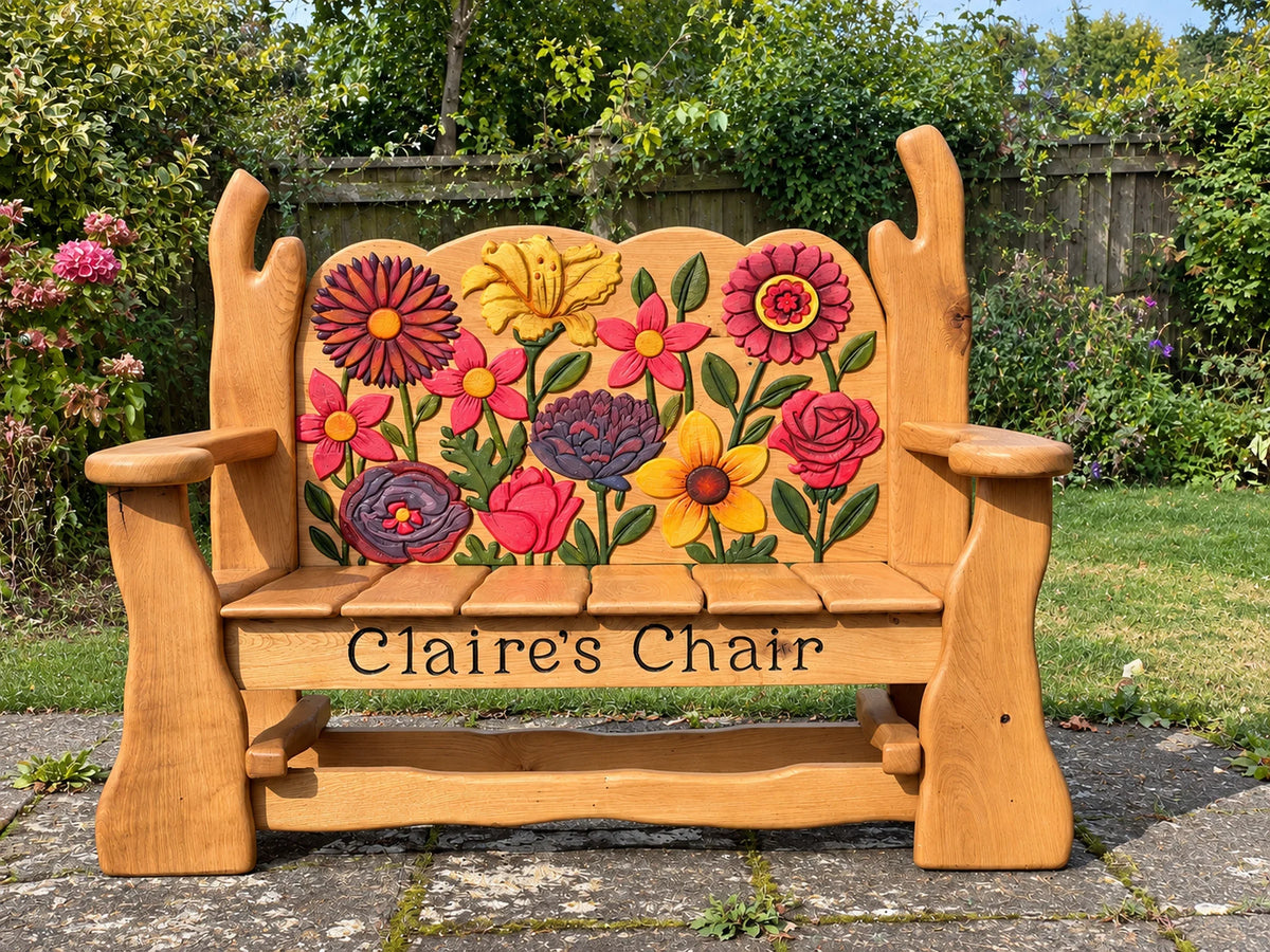 Solid oak memorial bench carved with daisies, roses, a lily and a peony, set on a garden patio
