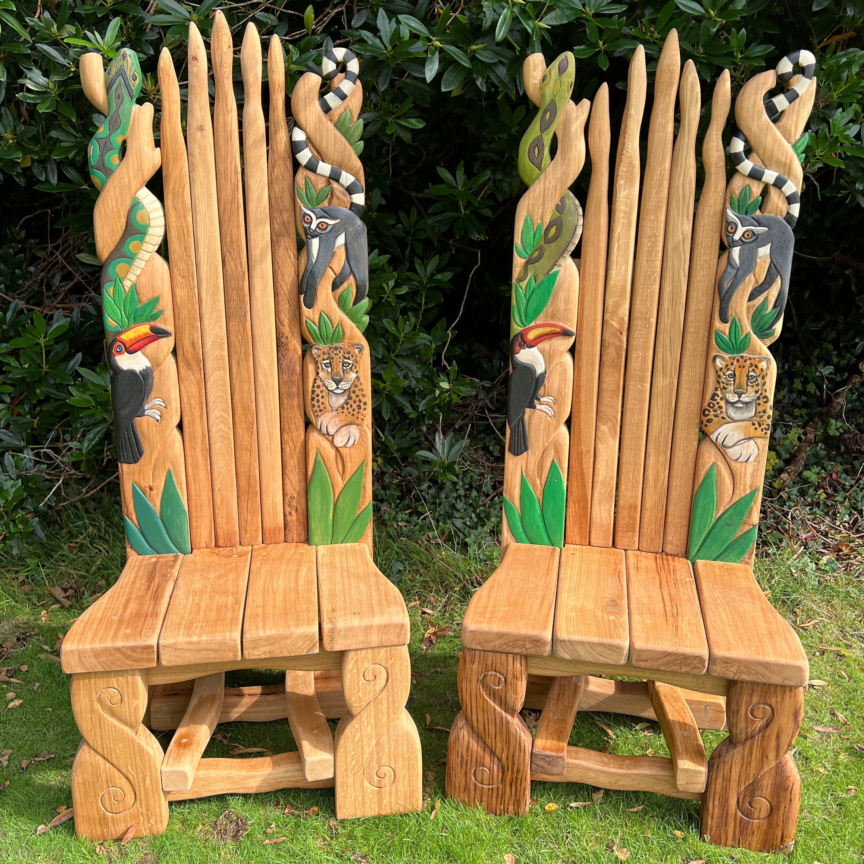 Two intricately carved wooden chairs with jungle animal designs, featuring lemurs, toucans, and leopards, set against a lush green background.