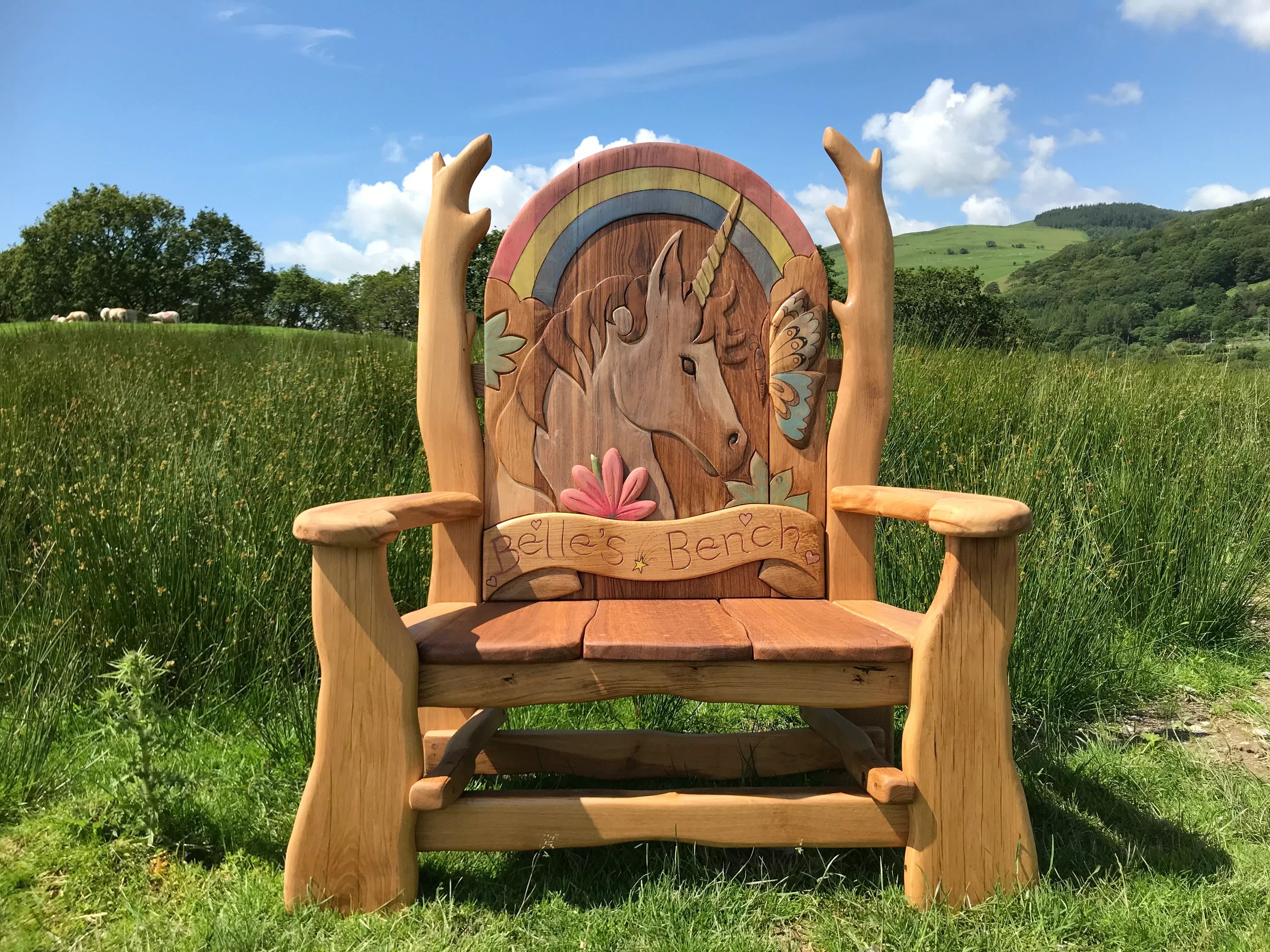 Handcrafted wooden bench with a custom horse design and vibrant rainbow carving, set in a scenic outdoor meadow. Ideal for gardens and memorials