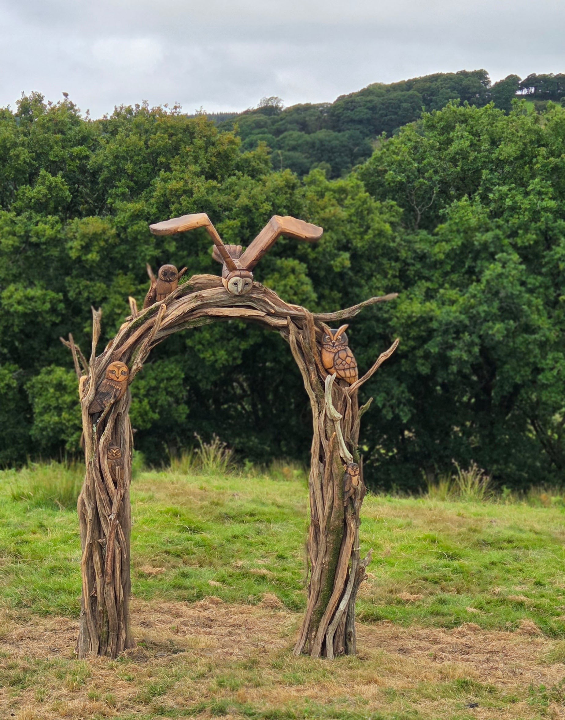 Wooden archway with owl sculptures in a natural setting