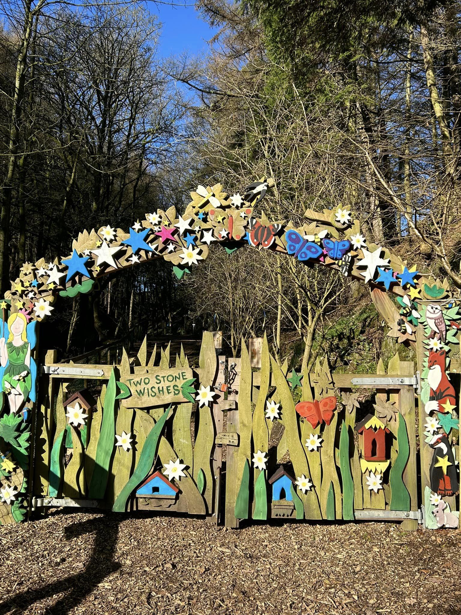Colorful wooden archway with garden-themed decorations in a forest setting