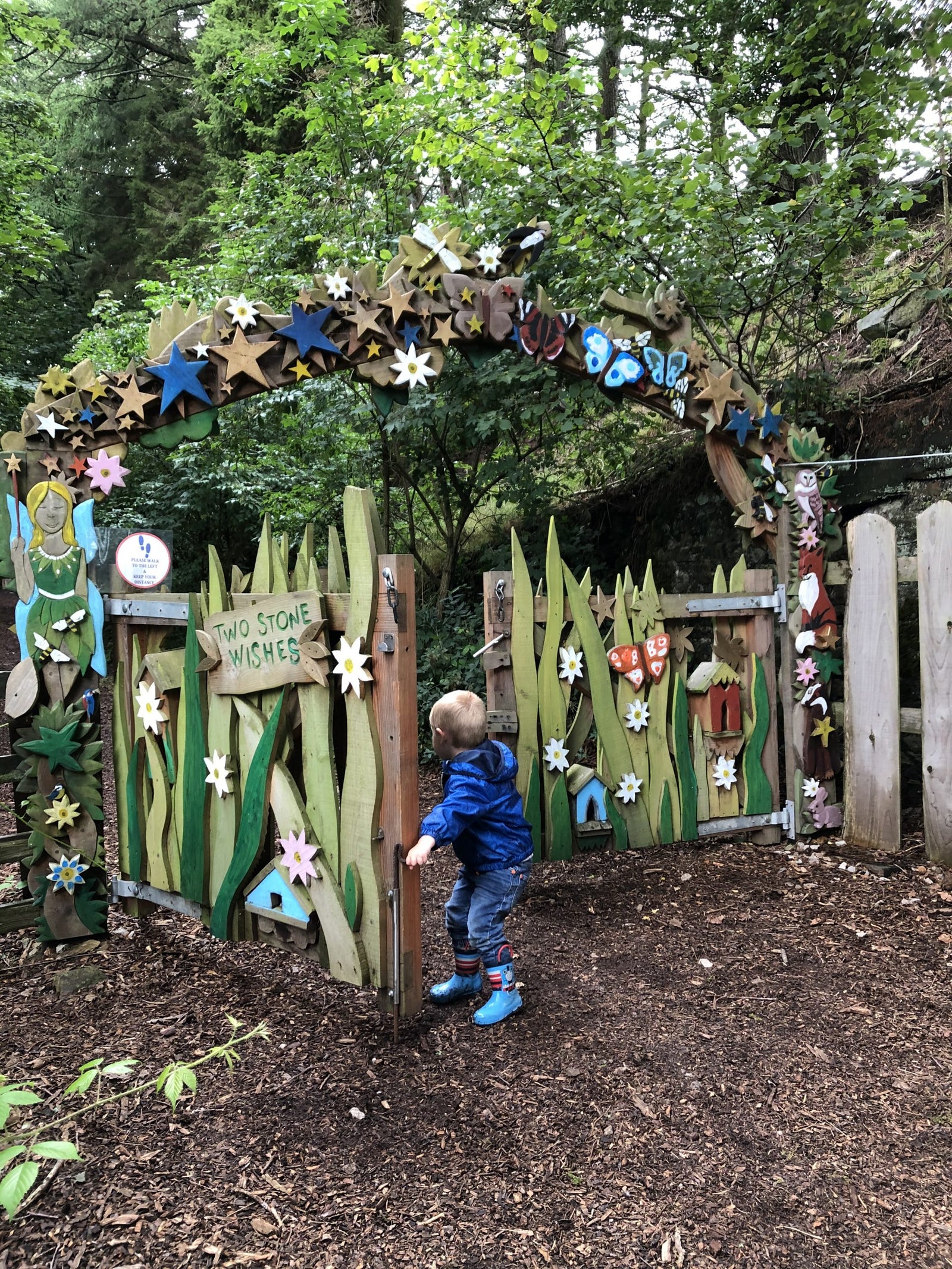 Child playing in a garden with a decorative wooden arch and fence.
