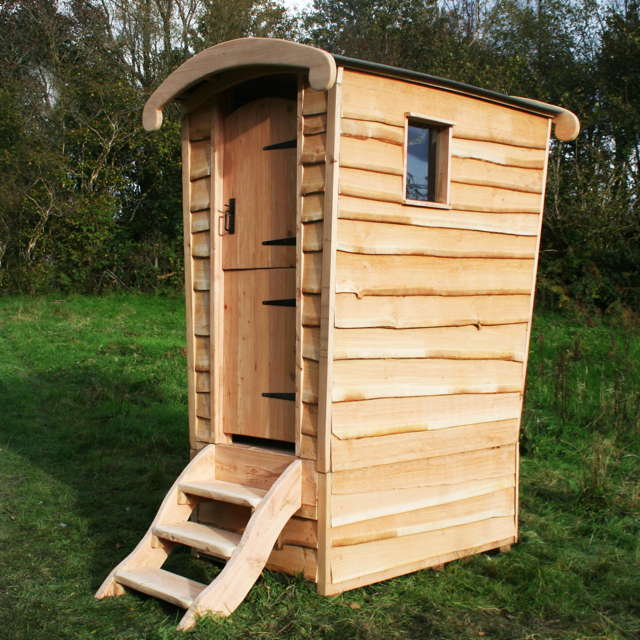 Gypsy Caravan Composting Toilet with a unique curved roof, wooden steps, and rustic cladding, set in a scenic outdoor environment, ideal for eco-friendly and remote use