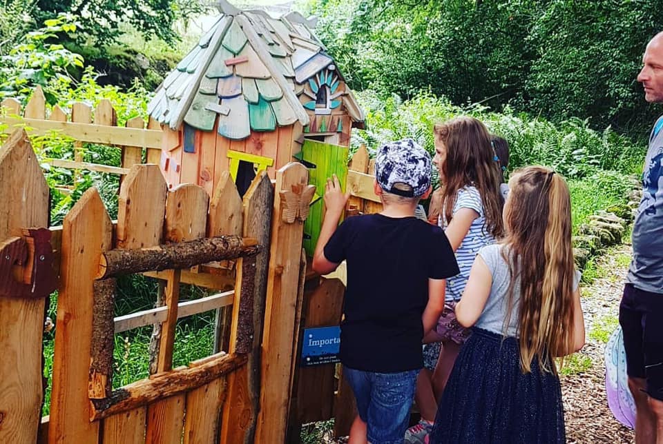 Children exploring a fairy house in a fenced area