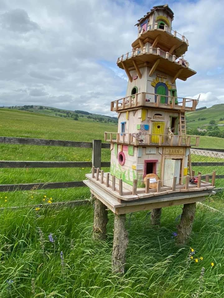 Tall fairy house with barn sign in a grassy field