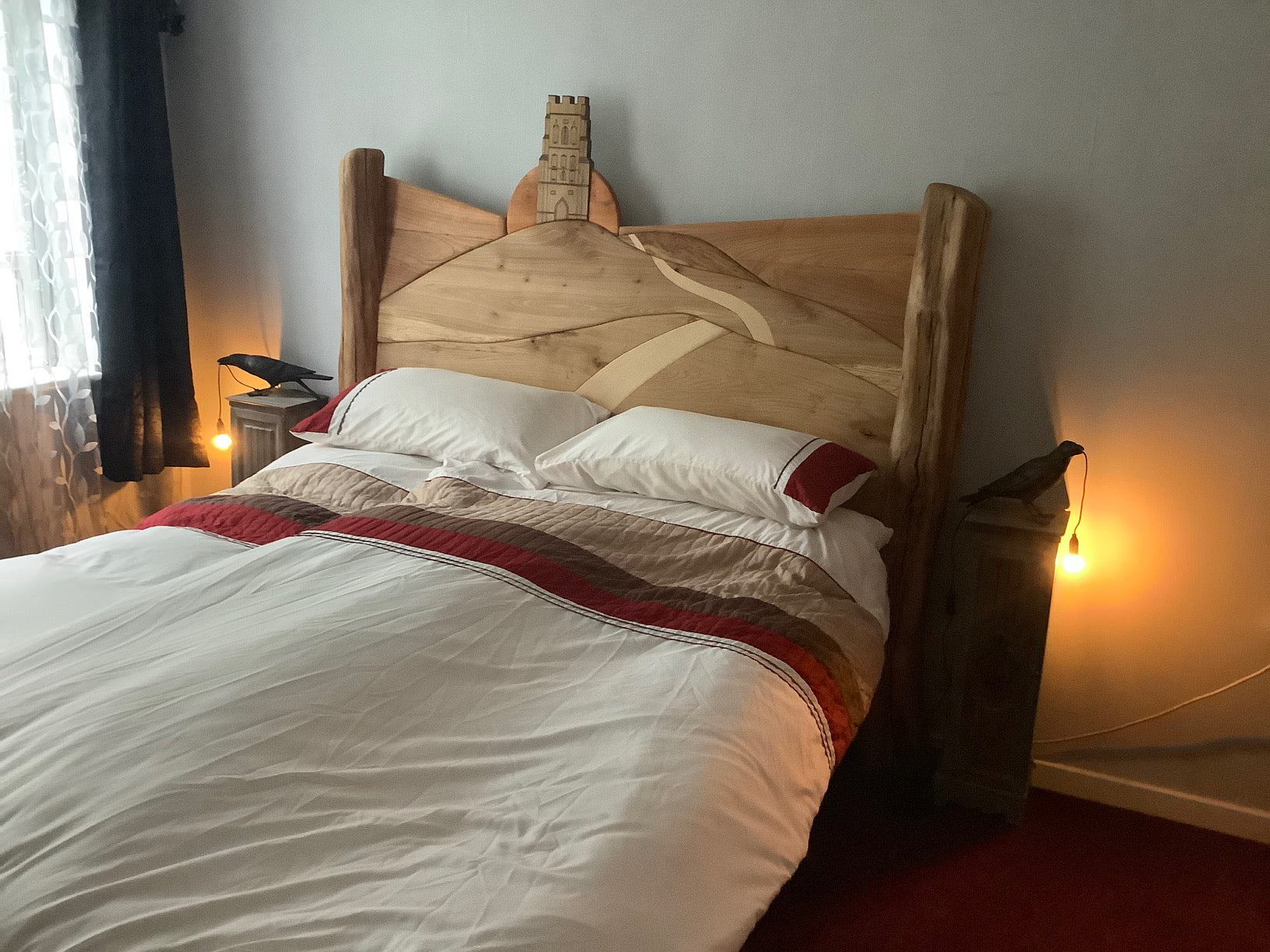 Front view of the Glastonbury Tor-inspired bed, showcasing hand-carved details of the Tor and path against a wooden sunrise background