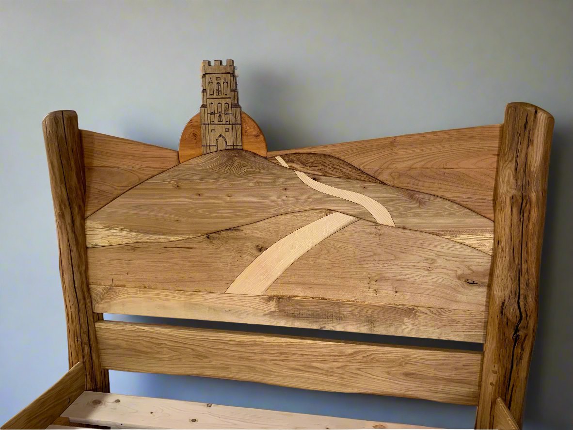 Detailed view of the hand-carved headboard on the Glastonbury Tor bed, featuring a carved path leading up to the Tor