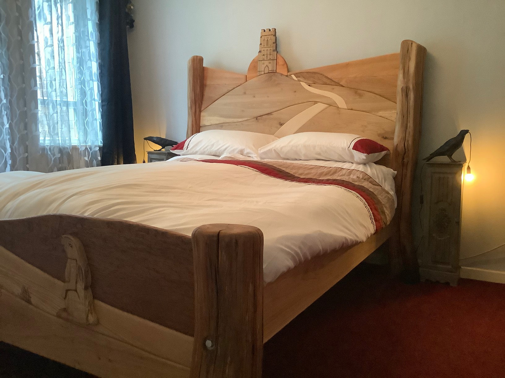 Glastonbury Tor bed frame displayed outdoors with lush green hills in the background, highlighting the natural wood and intricate carving