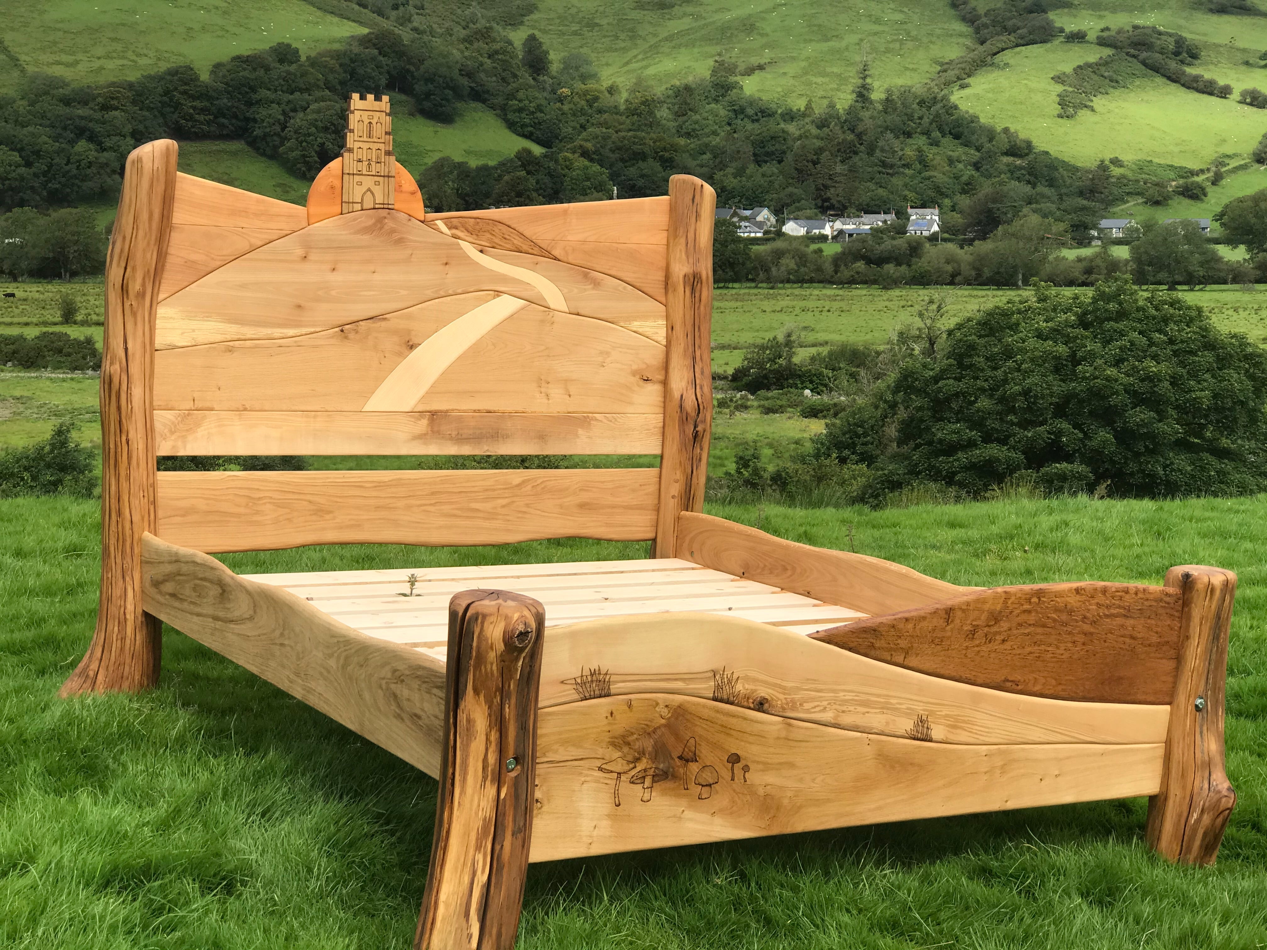 Glastonbury Tor bed with carved sunrise and path design, set against a rural landscape with green hills