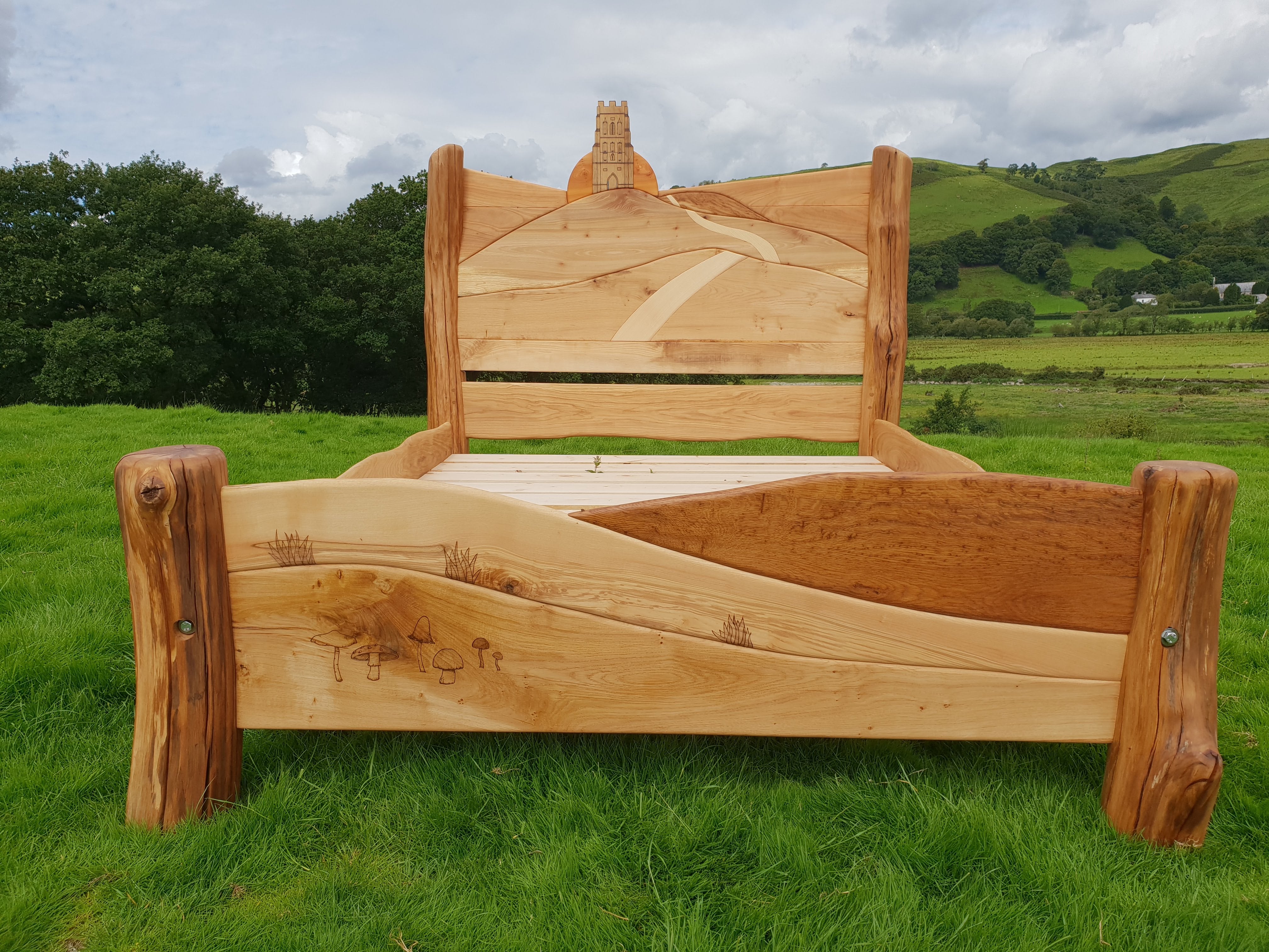 Glastonbury Tor bed with carved sunrise and path design, set against a rural landscape with green hills