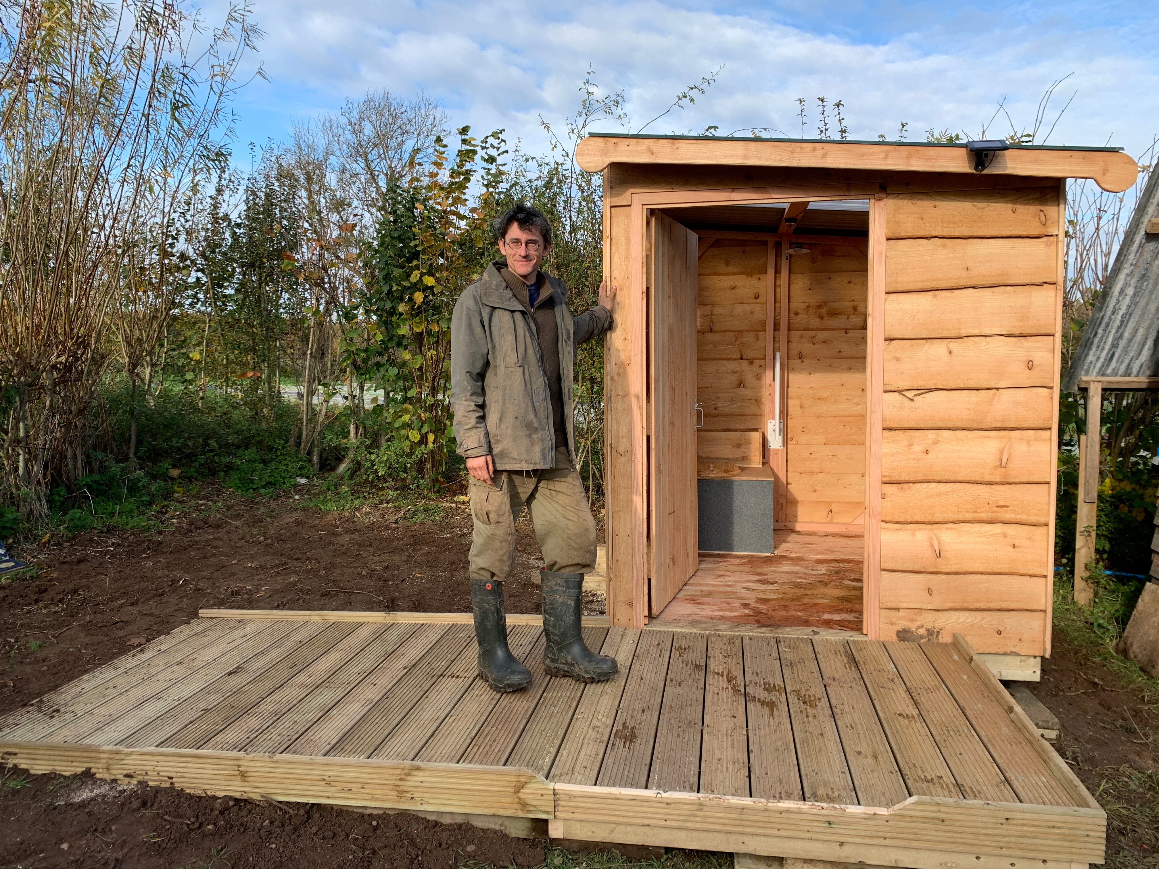 Man standing beside a wooden compost toilet