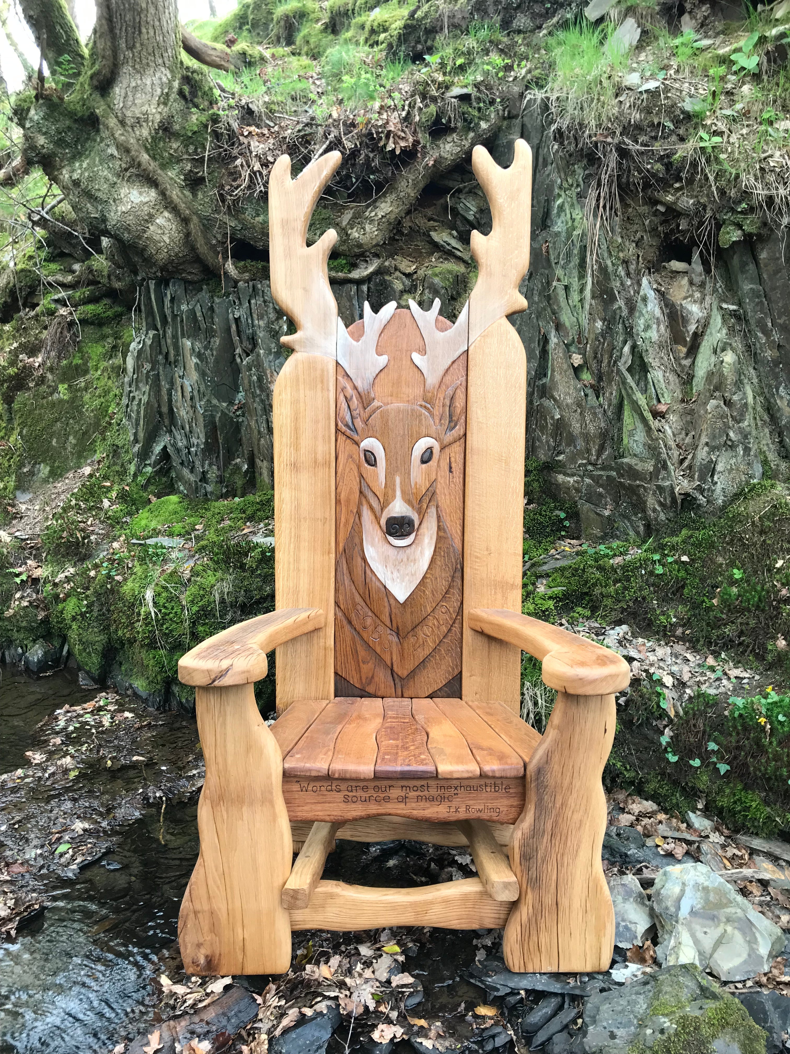 Wooden chair with deer carving by a stream.