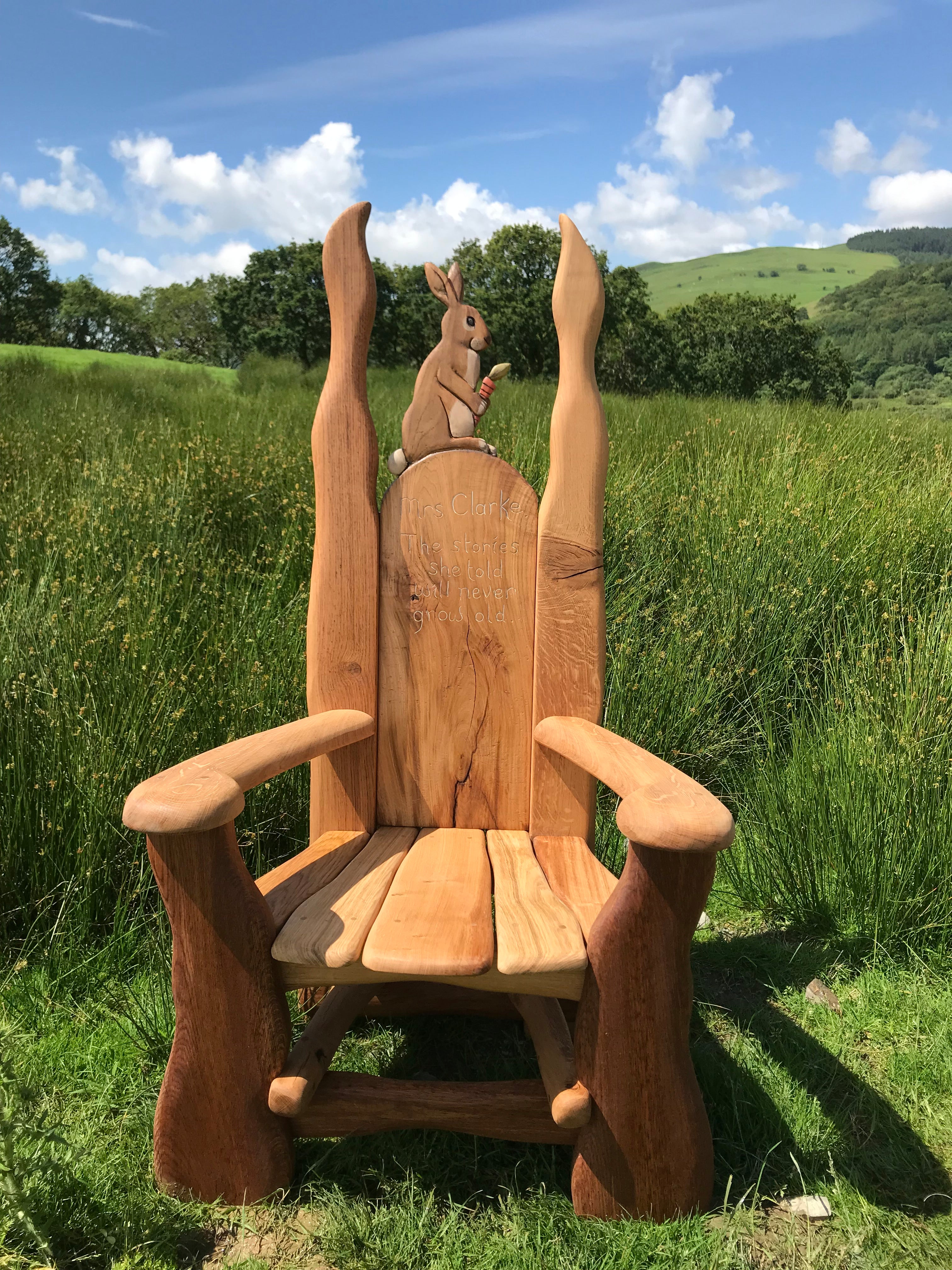 Wooden chair with rabbit carving in a grassy field.