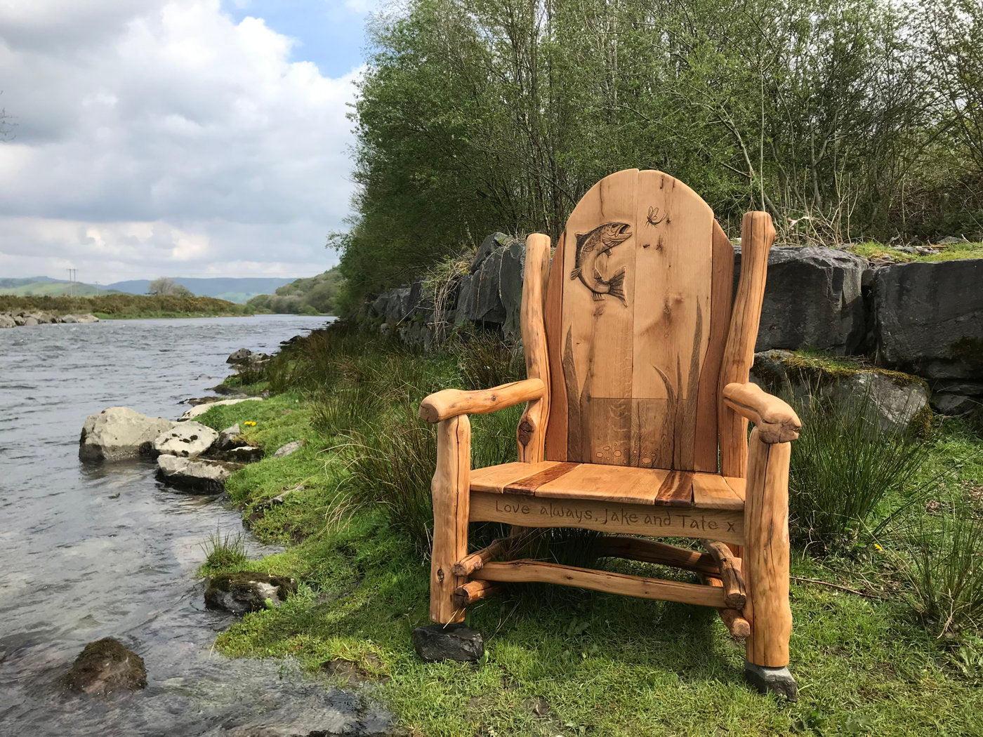 Rustic bench by a river with fish carving and message.