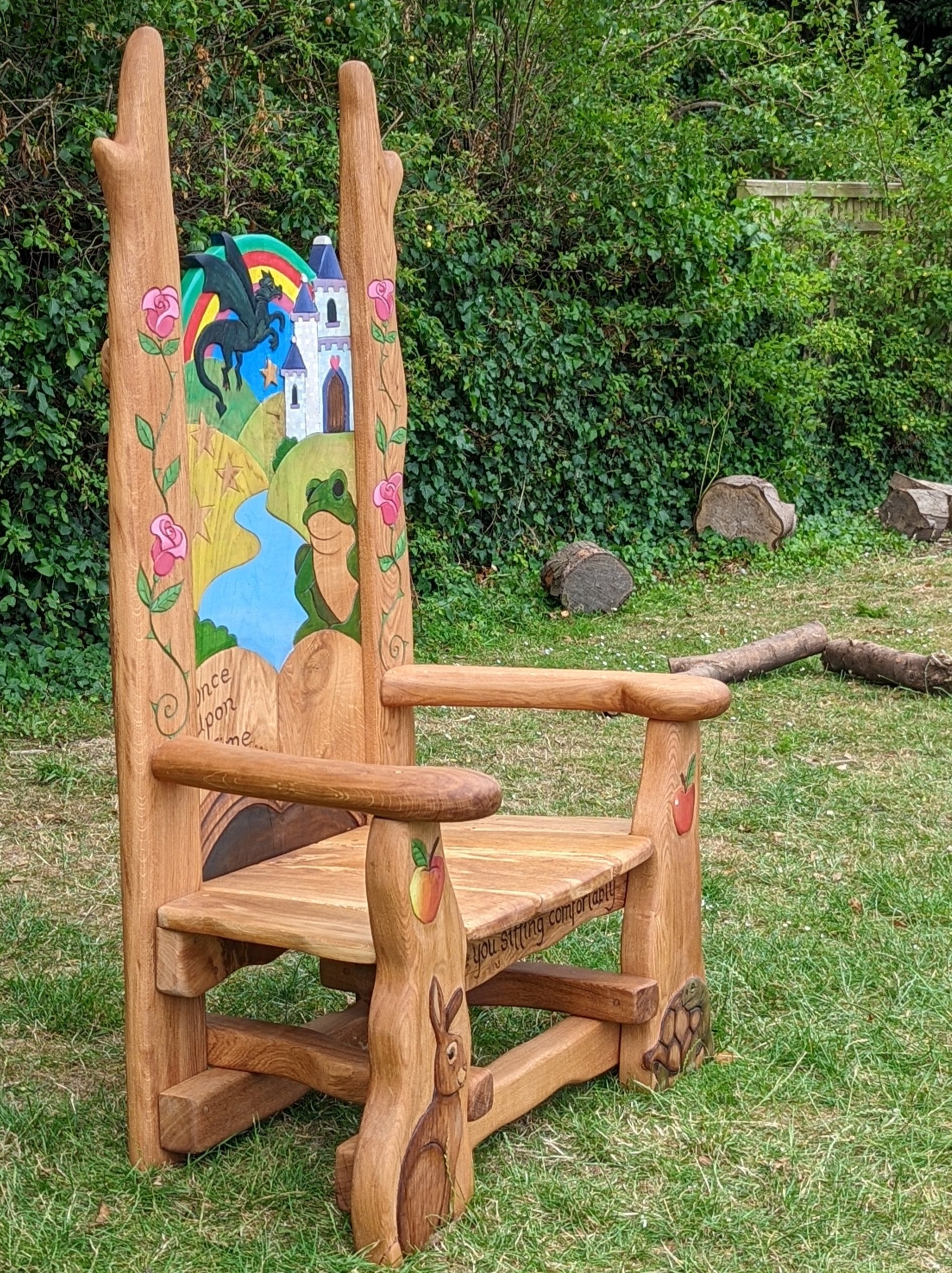 Handcrafted wooden storytelling chair featuring a colorful 'Once Upon a Time' theme with a castle, dragon, and frog design, surrounded by carved roses, apples, a rabbit, and a tortoise, perfect for inspiring imagination