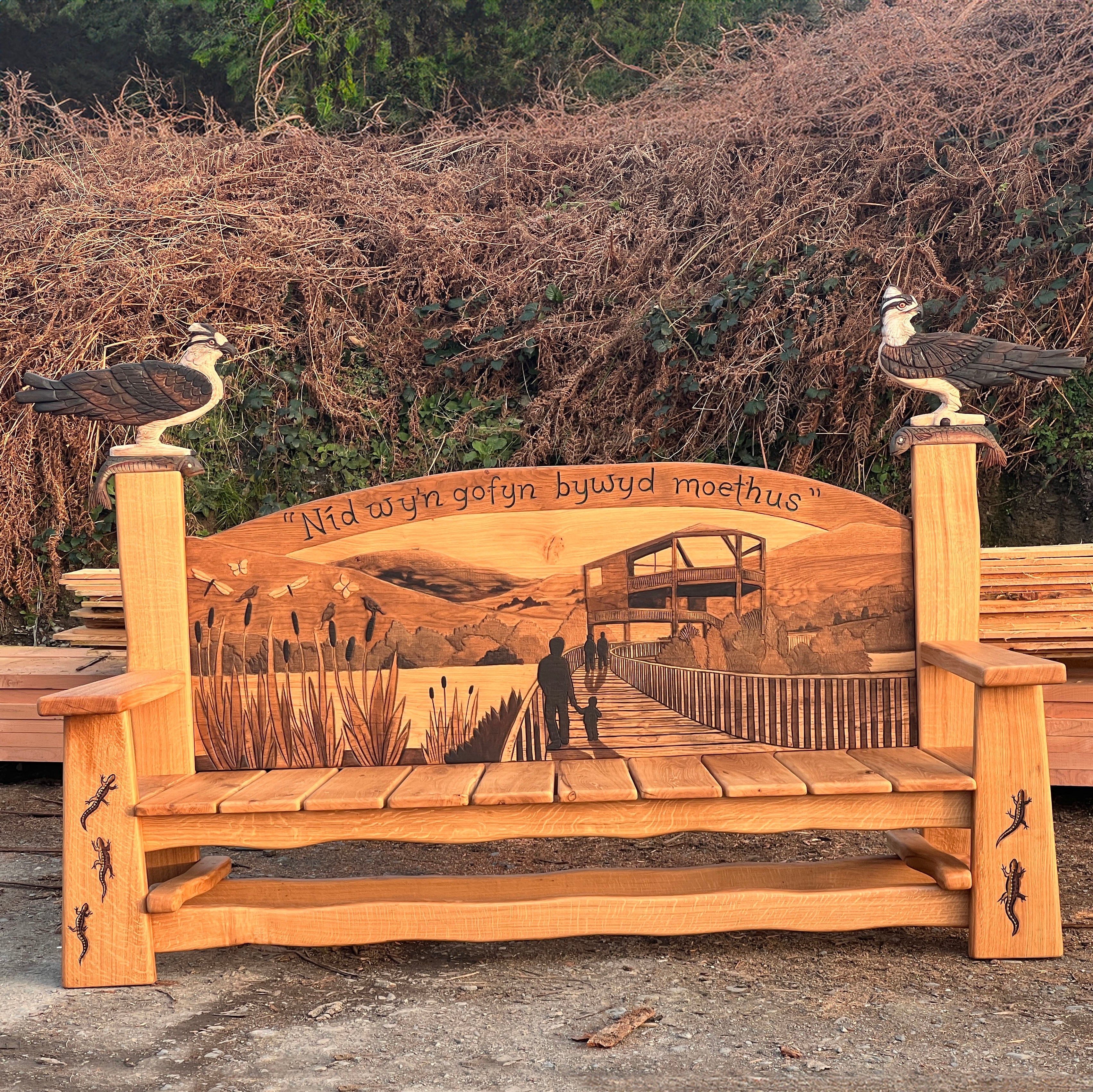 Full view of carved oak Ospreys Bench, 195cm wide, with osprey carvings on each side at Cors Dyfi Wildlife Hide