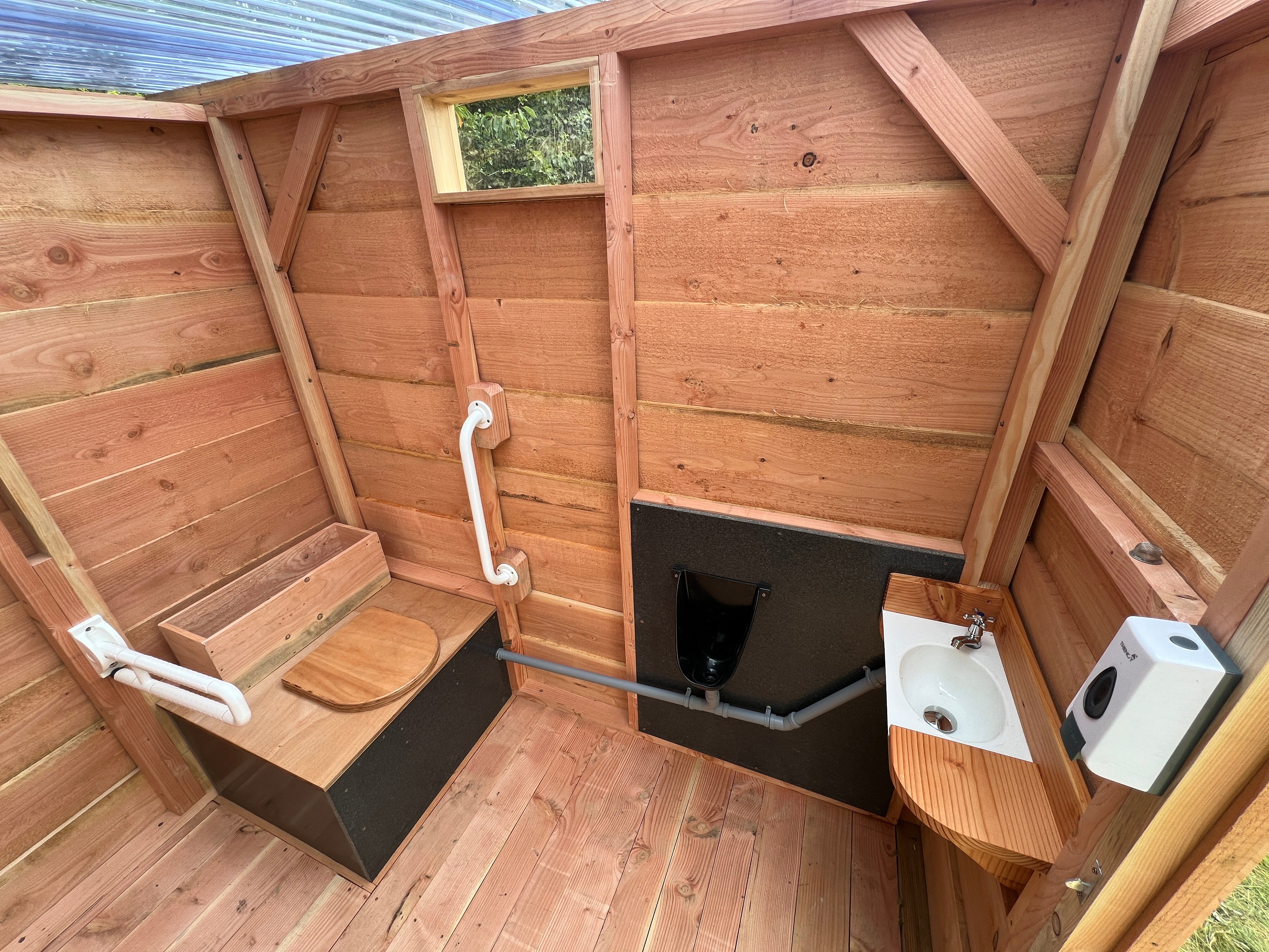 Interior view of an accessible compost toilet with grab bars, urinal, and sink, designed by Free Range Designs for eco-friendly and accessible sanitation