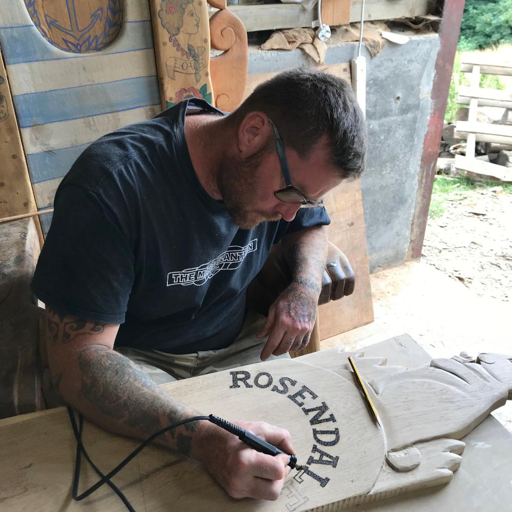 Artisan at Free Range Designs engraving intricate lettering into wood, showcasing skilled craftsmanship and attention to detail