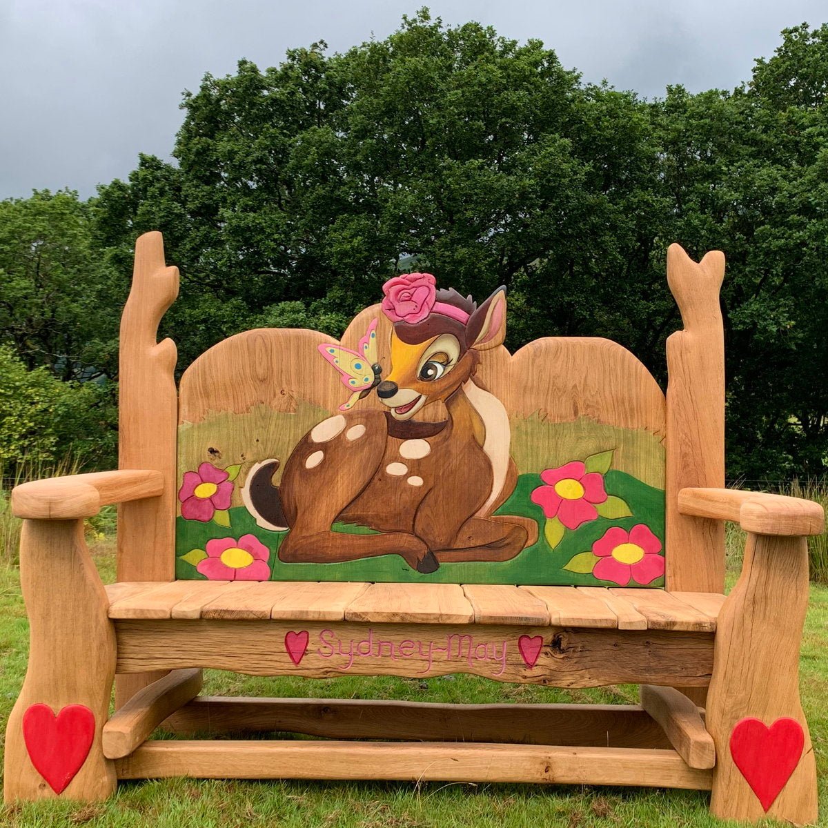 A handcrafted Bambi-themed memorial oak bench with vibrant carvings, featuring a lovingly detailed Bambi design, perfect for outdoor spaces or as a tribute to cherished memories.

