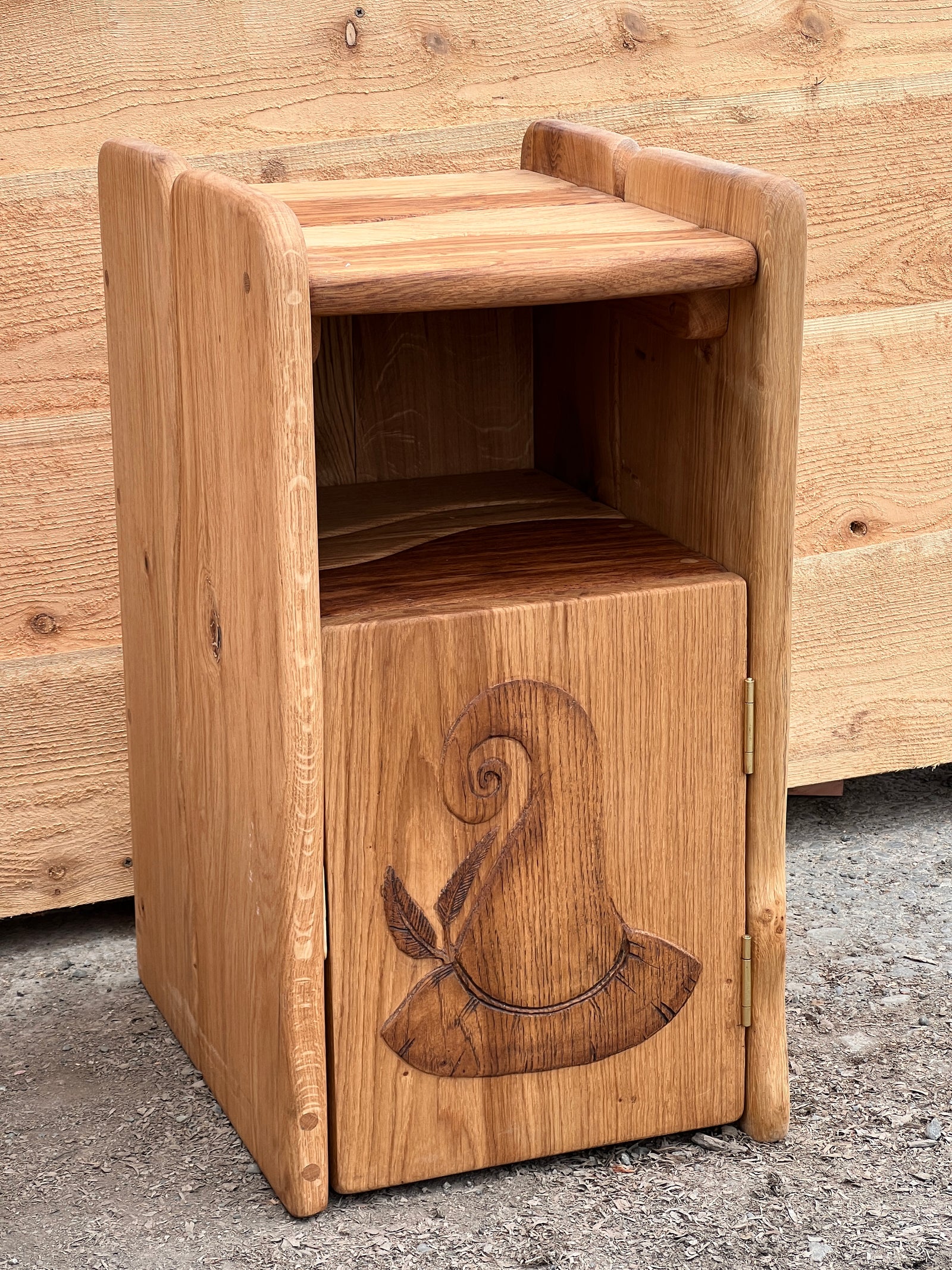 Solid oak bedside cabinet with hand-carved door panel and open shelf — front view showing wood grain detail