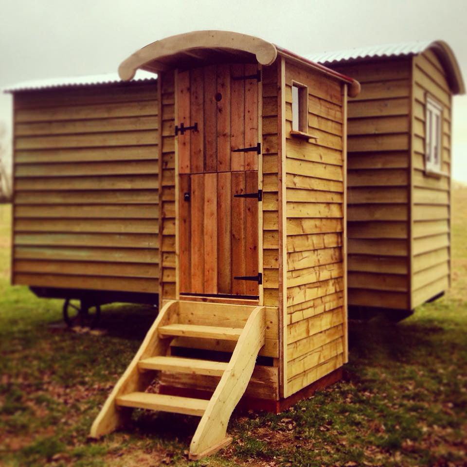 Wooden composting toilet with steps in a grassy area and shepherd's hut — handmade eco outdoor facility, Wales