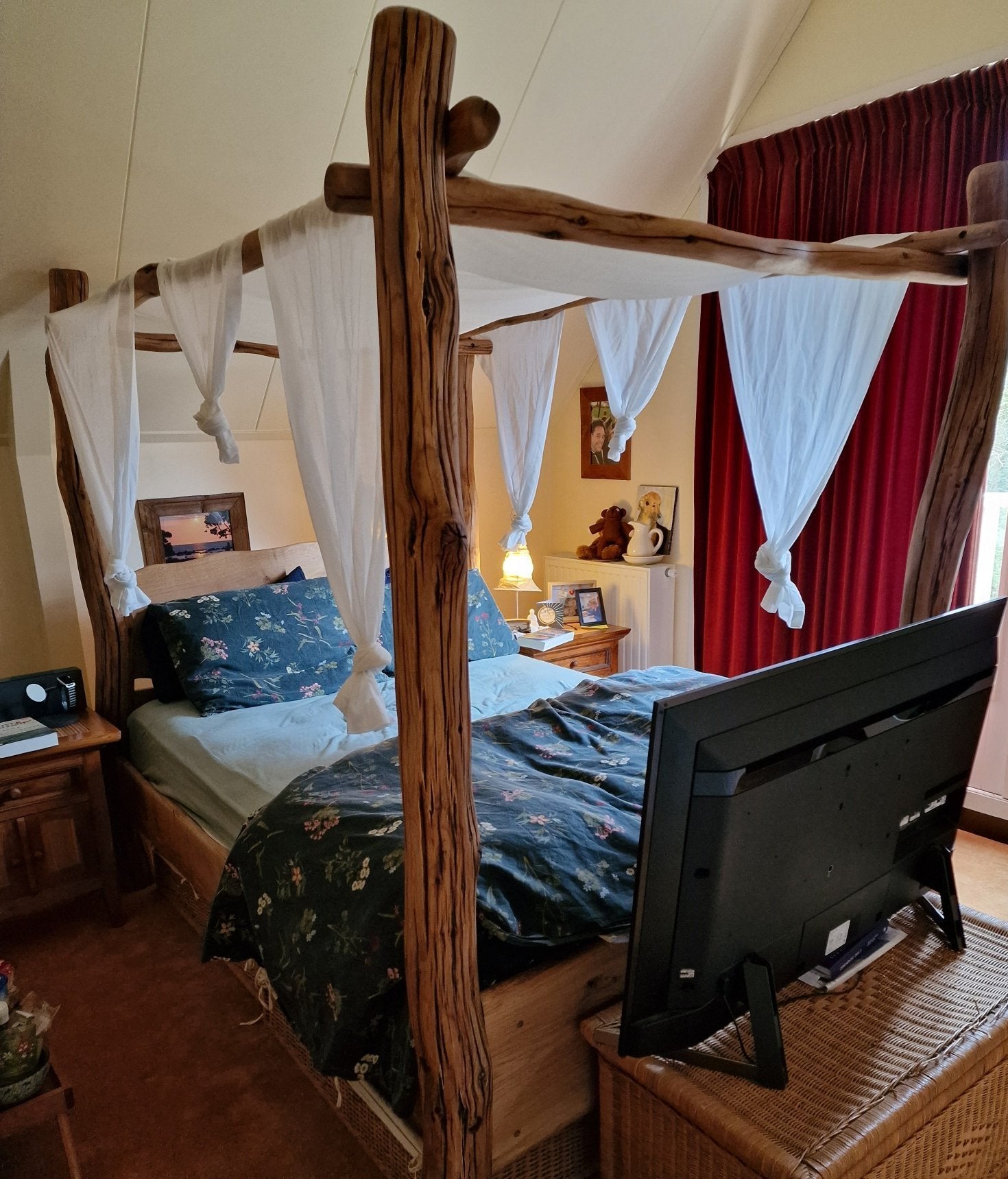 Handcrafted four-poster canopy bed frame with natural wood finish and white canopy drapes, creating a cozy and serene bedroom setup for Brenda