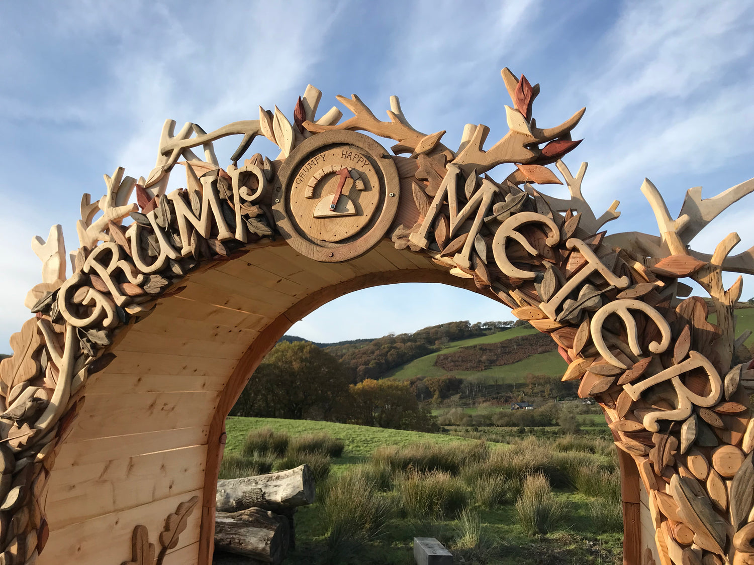 Wooden arch with carved letters and antlers against a natural landscape