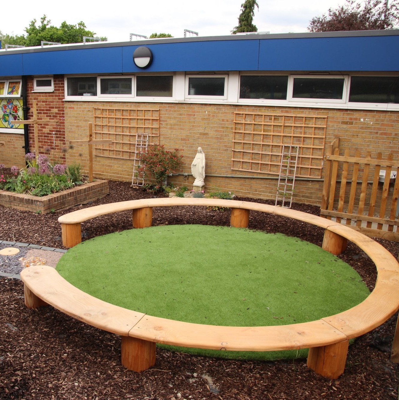 Wooden circular bench seating installed in a school playground, providing an inviting space for group activities and storytelling, surrounded by a landscaped garden area