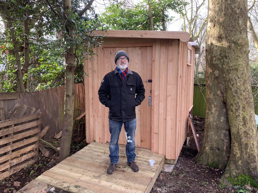 Man standing in front of a wooden compost toilet