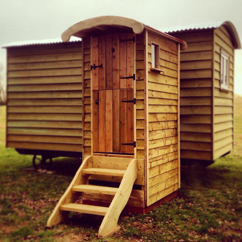 Wooden composting toilet with steps in a grassy area and shepherds hut 