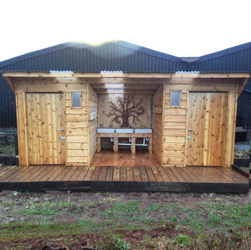 Dual compost toilet structure with integrated washroom and decorative tree mural, crafted by Free Range Designs for eco-friendly public spaces