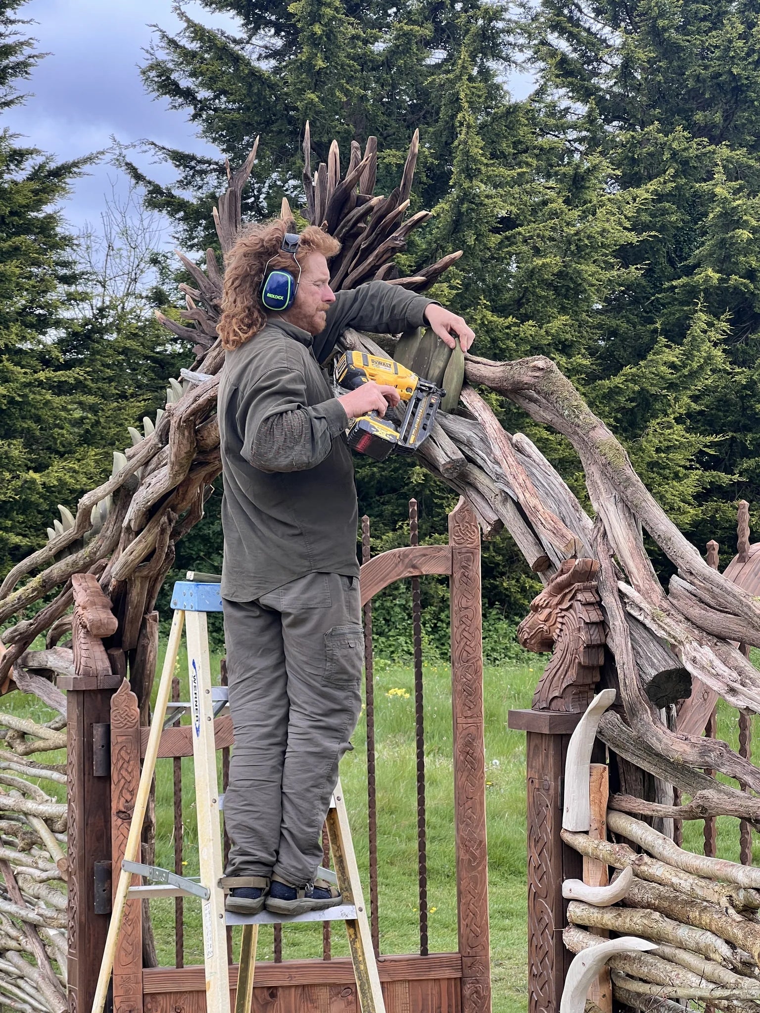 Full view of dragon driftwood archway from left showing spine fins and open wooden gate with twisted spindles