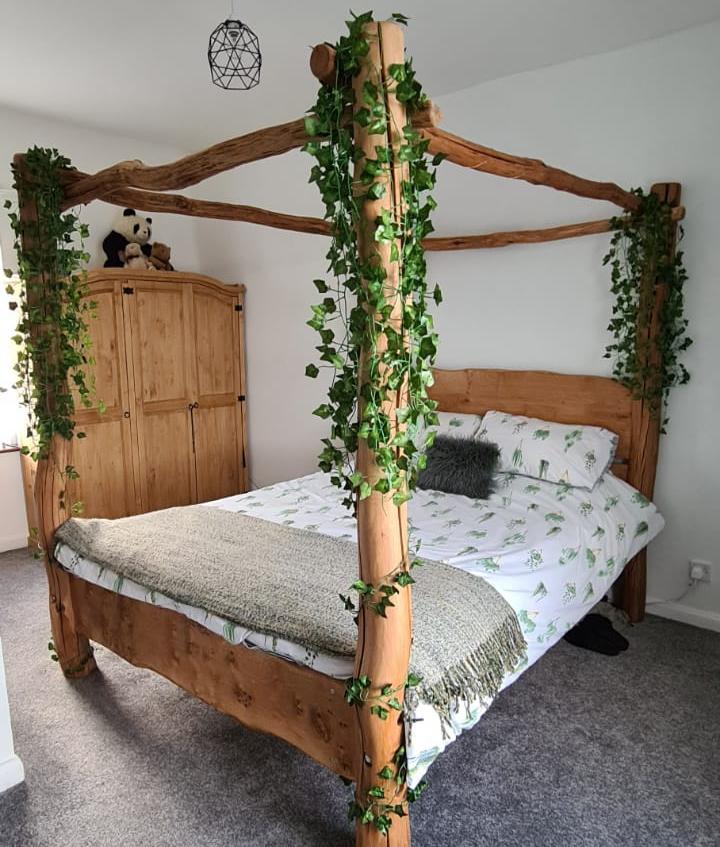 Handcrafted four-poster bed adorned with greenery vines, creating a natural and dreamy aesthetic for a cozy bedroom setting