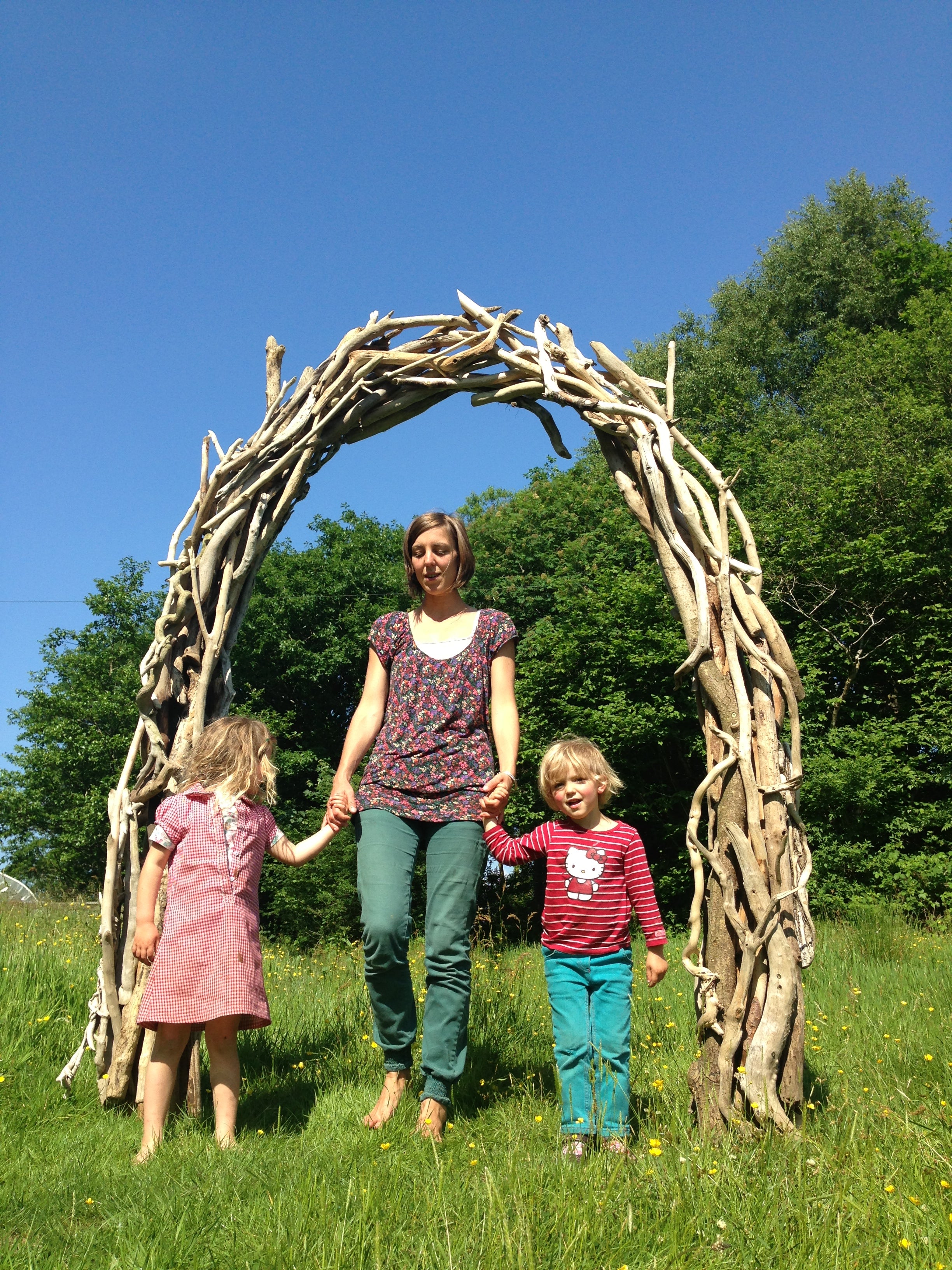 Woman and two children standing under a driftwood wooden arch