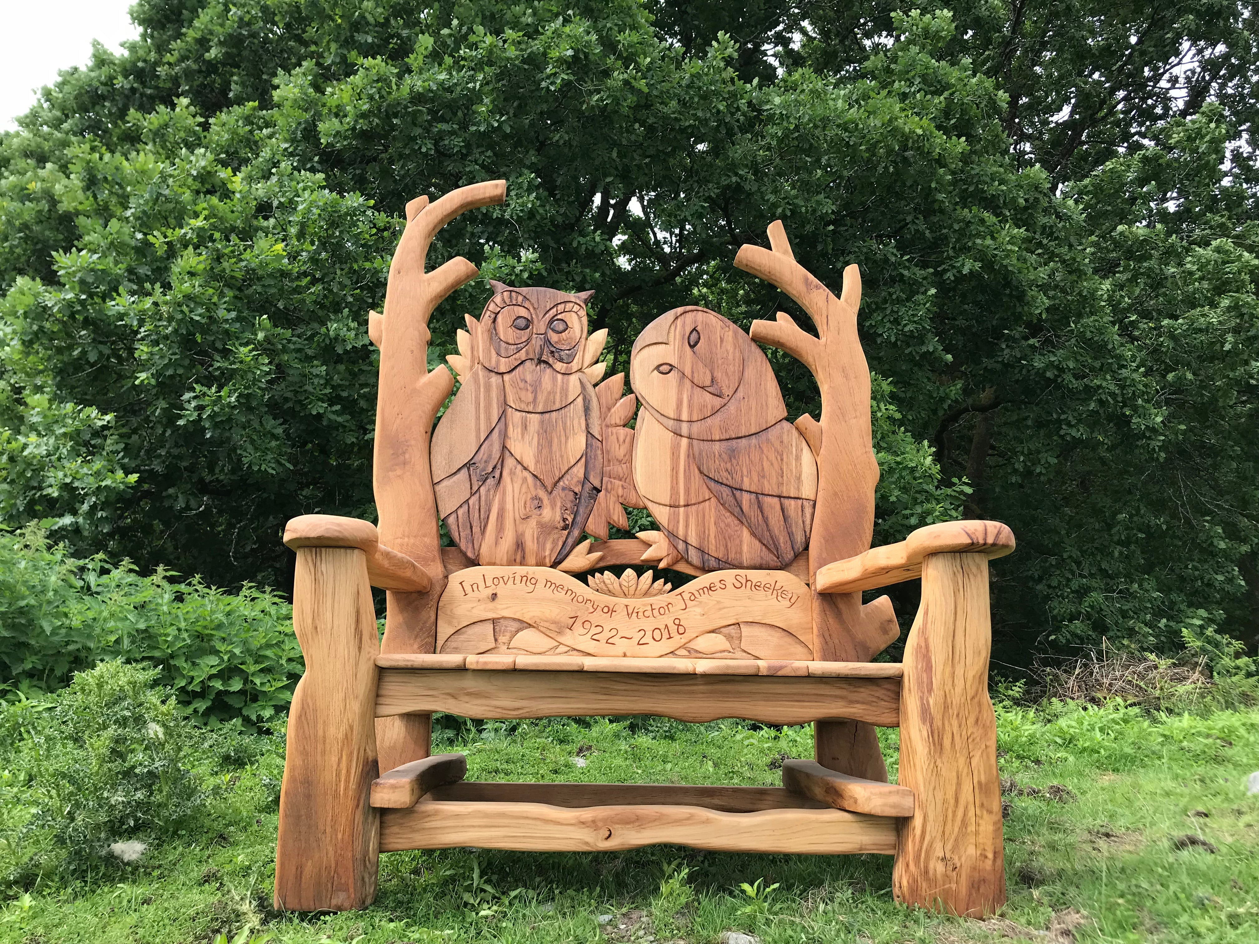 Banc commémoratif en bois avec des sculptures de hibou dans la nature.